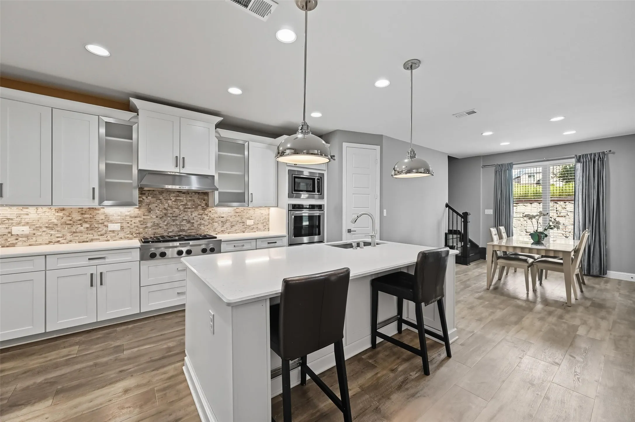 Contemporary kitchen featuring white cabinetry, a large center island with seating, stainless steel appliances, a mosaic tile backsplash, and wood-finish flooring