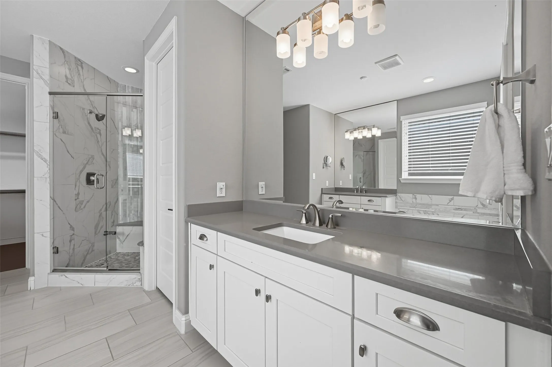 Spacious bathroom featuring a dual vanity with a gray countertop, white cabinetry, and brushed nickel hardware