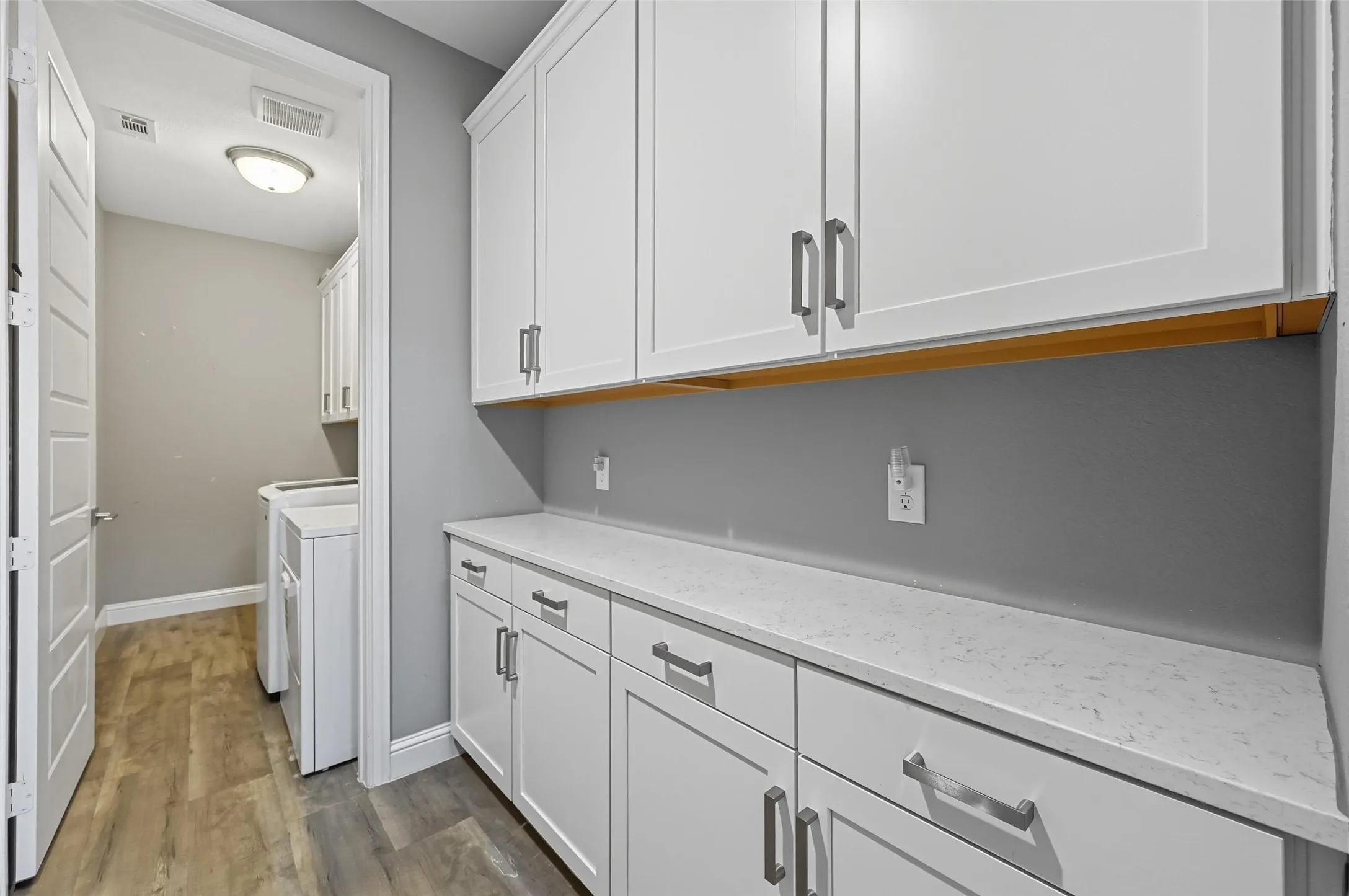 Bright laundry area featuring extensive white shaker cabinetry, light-toned countertops, wood-finish flooring, and a recessed ceiling light fixture