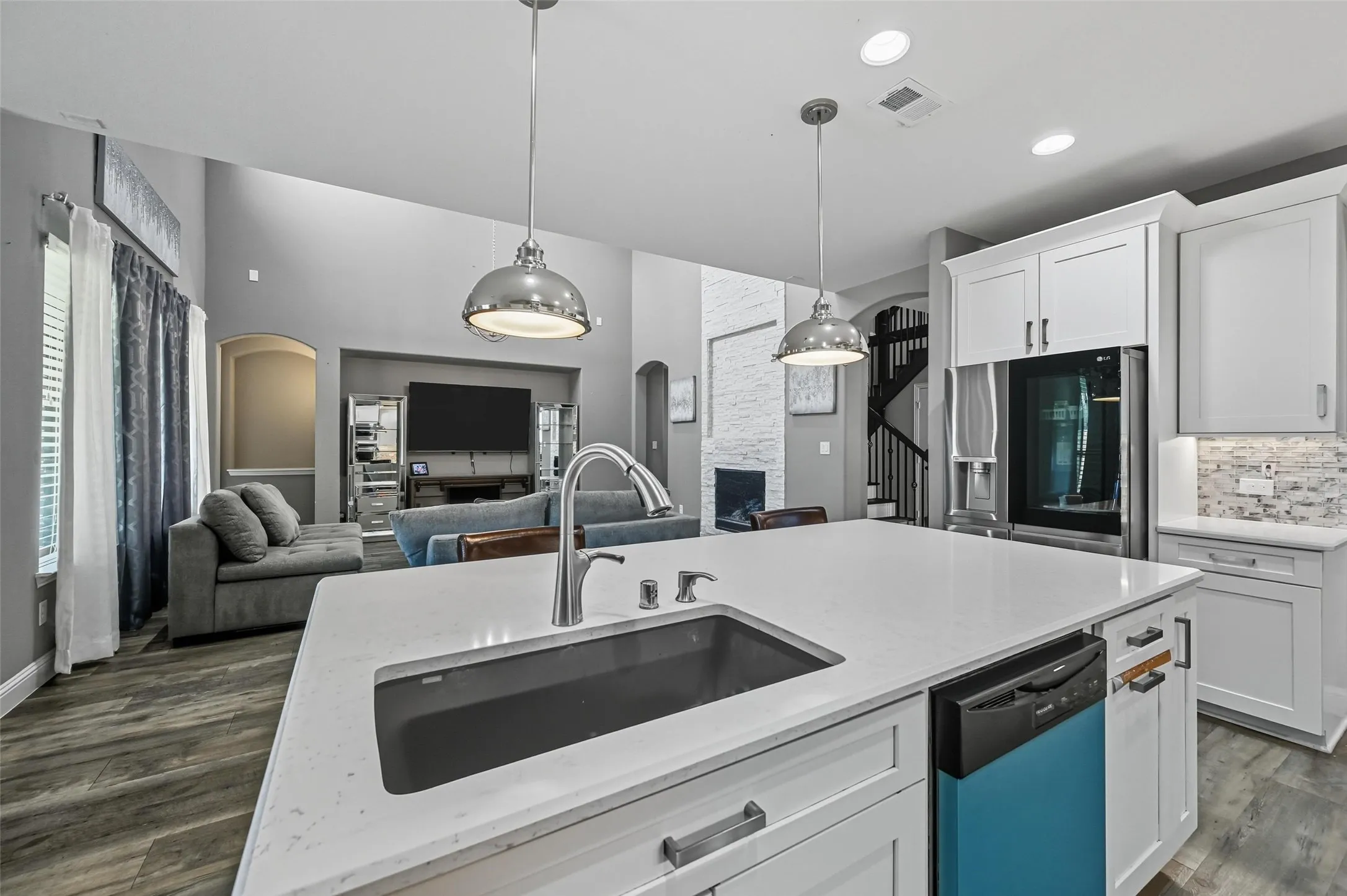Open-concept kitchen featuring a large island with an undermount sink, pendant lighting, white cabinetry, and wood-finish flooring