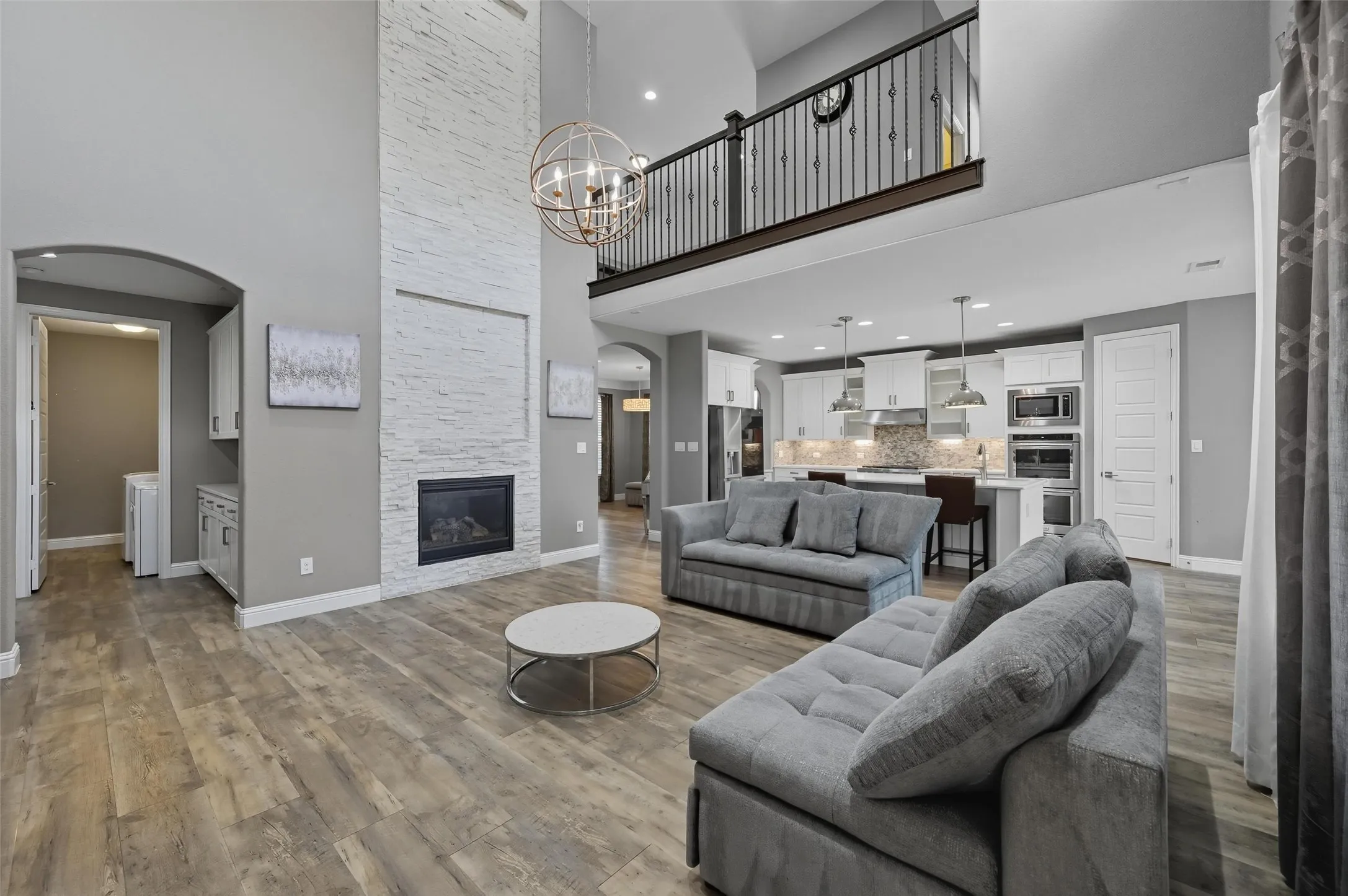 Spacious living area featuring a two-story ceiling, wood-finish flooring, and a floor-to-ceiling white stone fireplace with an integrated electric insert