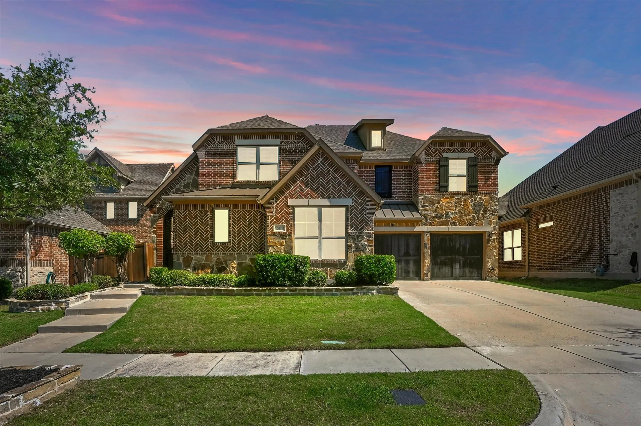 Brick and stone facade featuring a two-car garage, manicured lawn, and concrete driveway