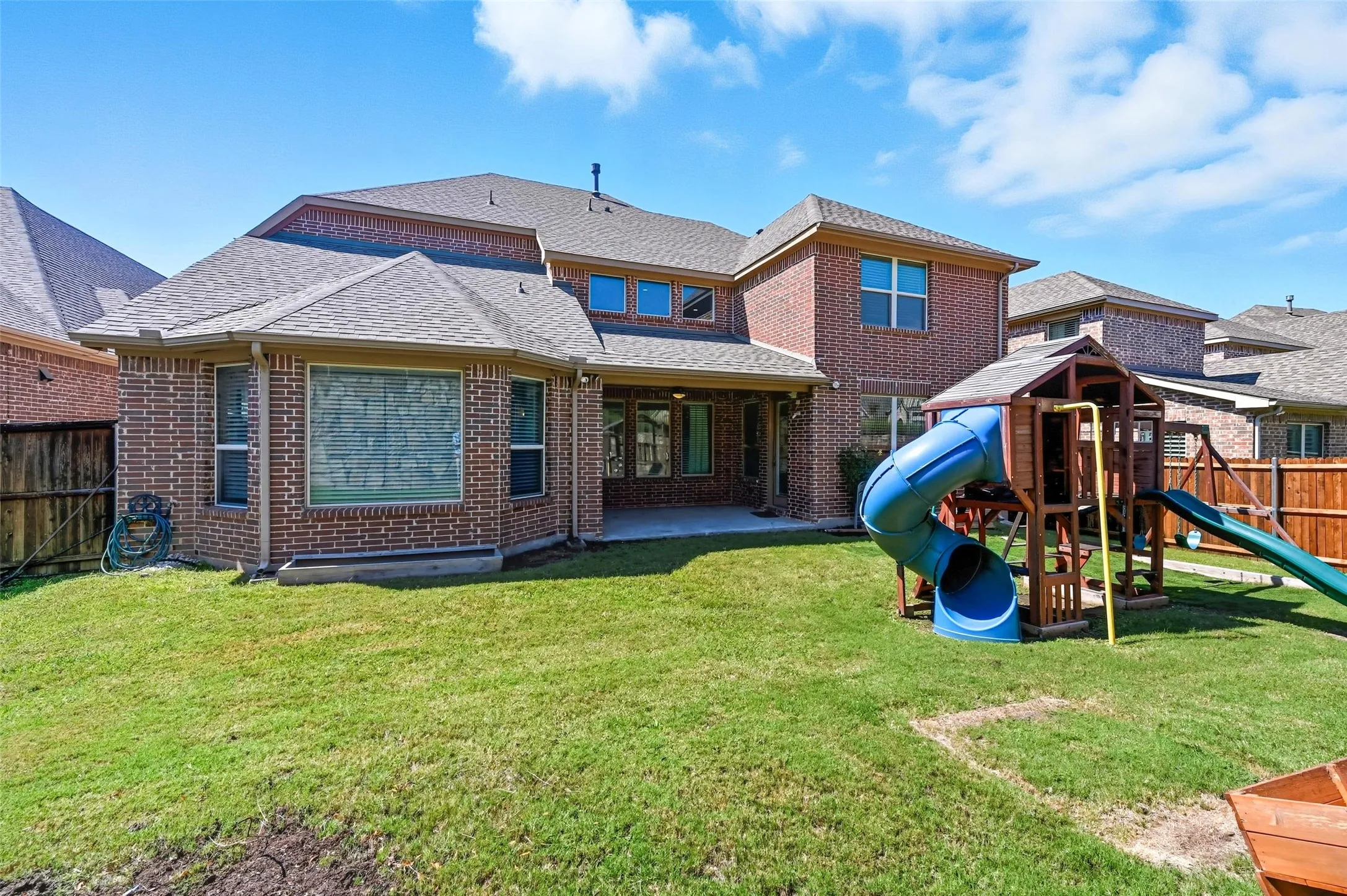 Expansive backyard featuring a brick exterior, covered patio, multiple windows, and a wood privacy fence