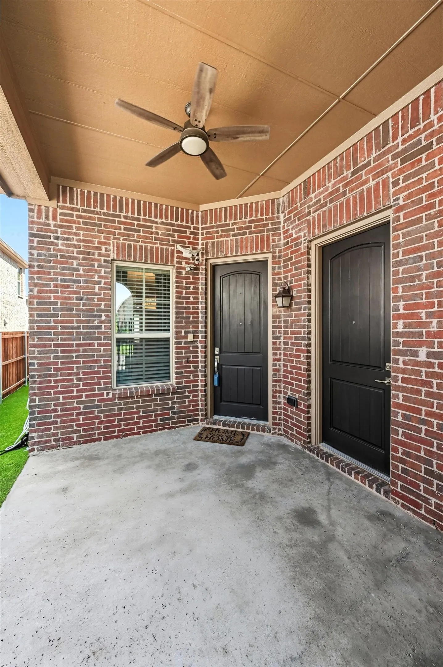 Covered patio featuring red brick exterior walls, concrete flooring, and ceiling-mounted fan with integrated lighting