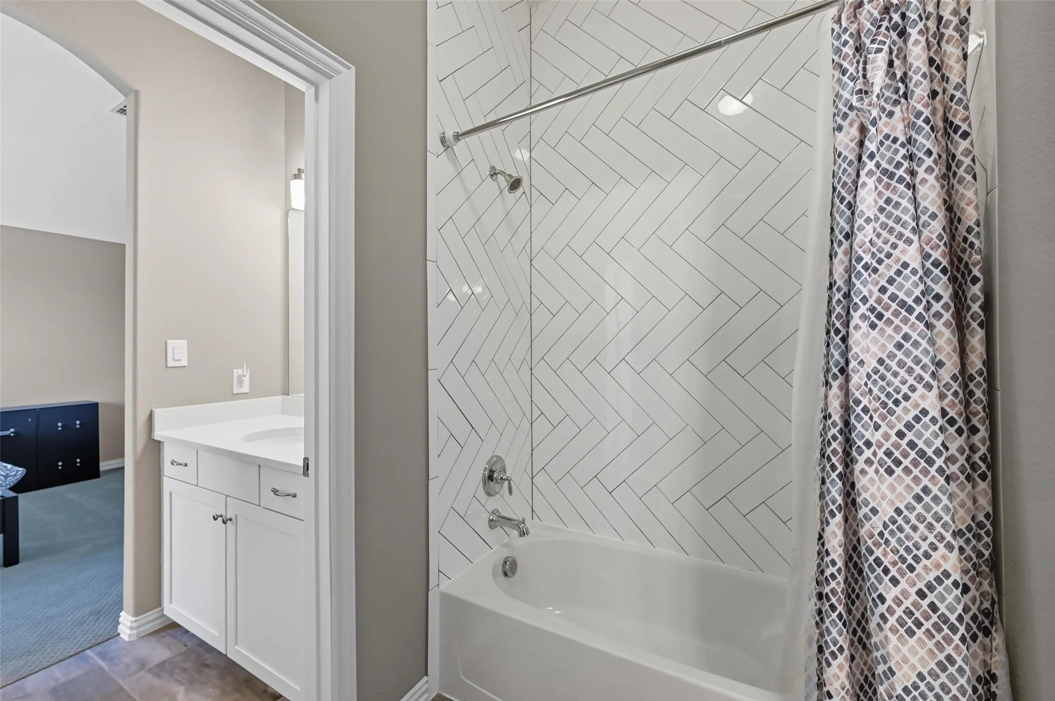Bathroom featuring a white bathtub, herringbone pattern tile surround, chrome fixtures, and a vanity with a white countertop and base cabinetry