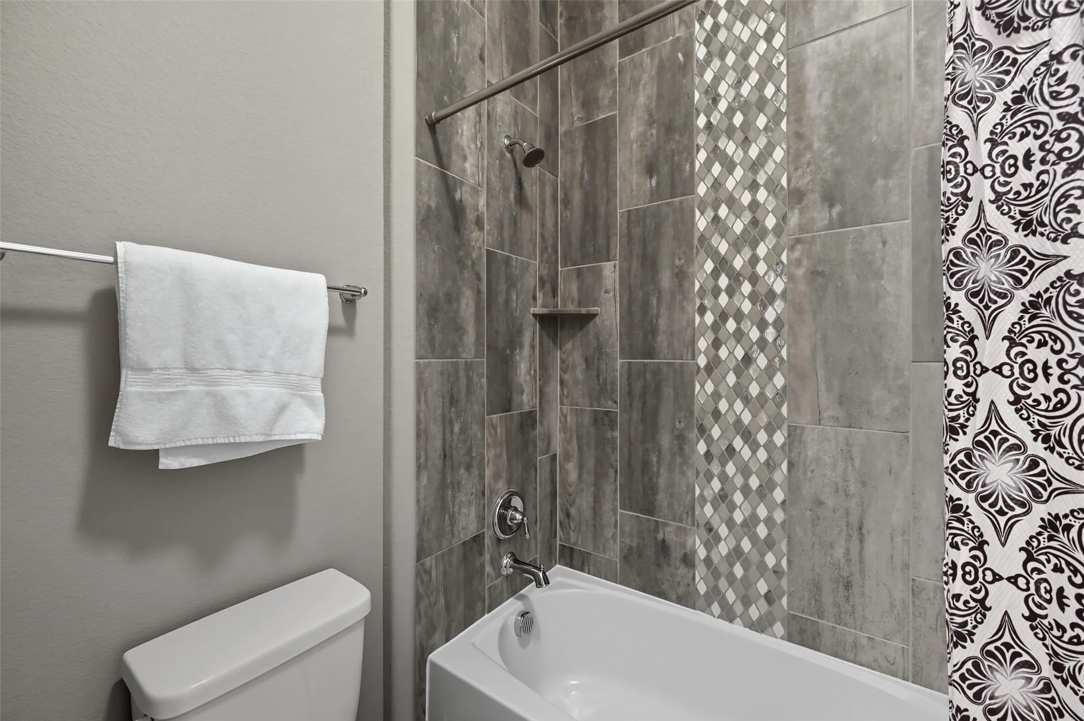 Bathtub-shower combination featuring wood-look tile surround with a mosaic accent strip and an integrated shower niche