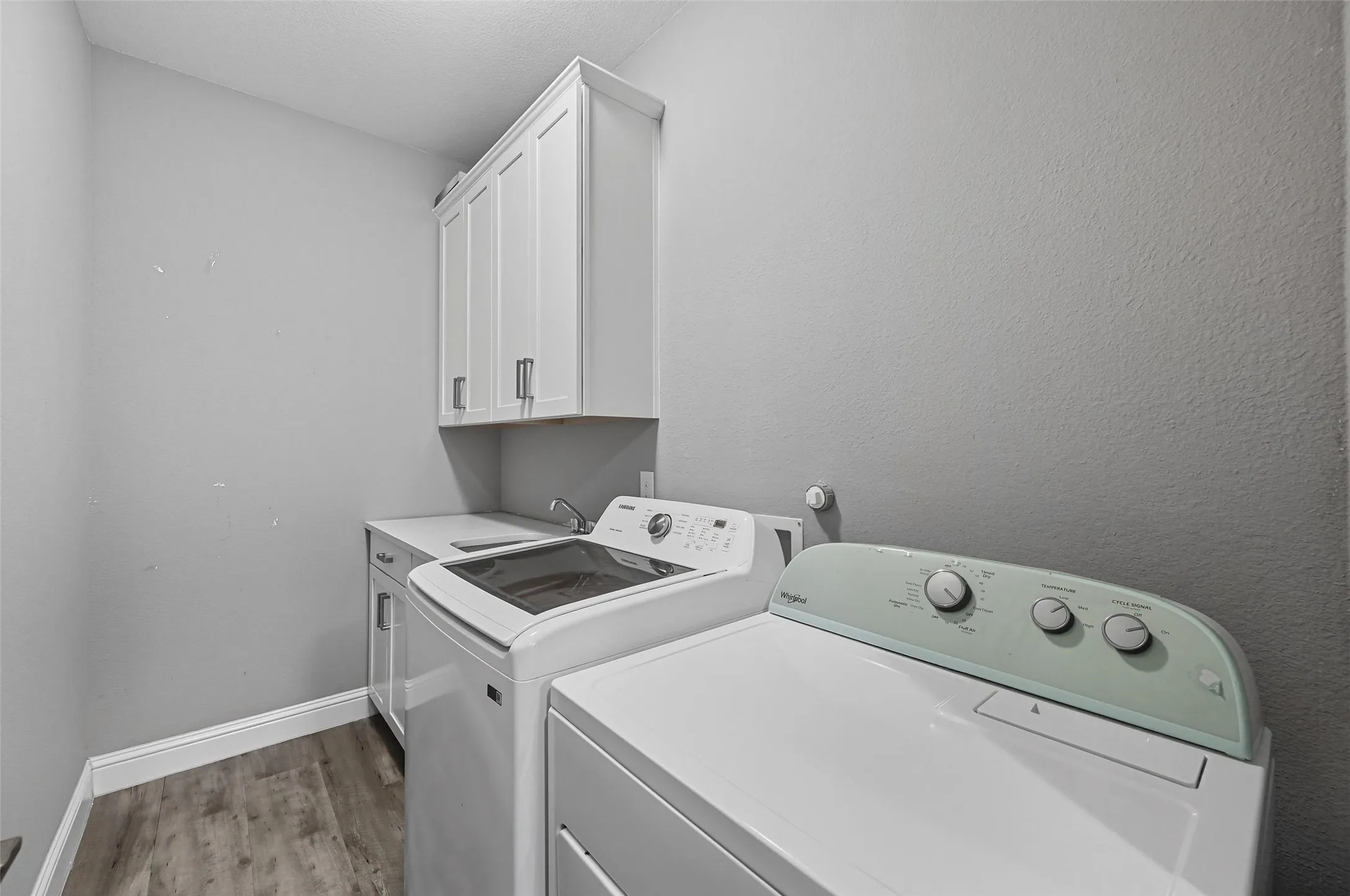 Laundry area featuring wood-finish flooring, white cabinetry with contemporary hardware, a utility sink, and ample counter space