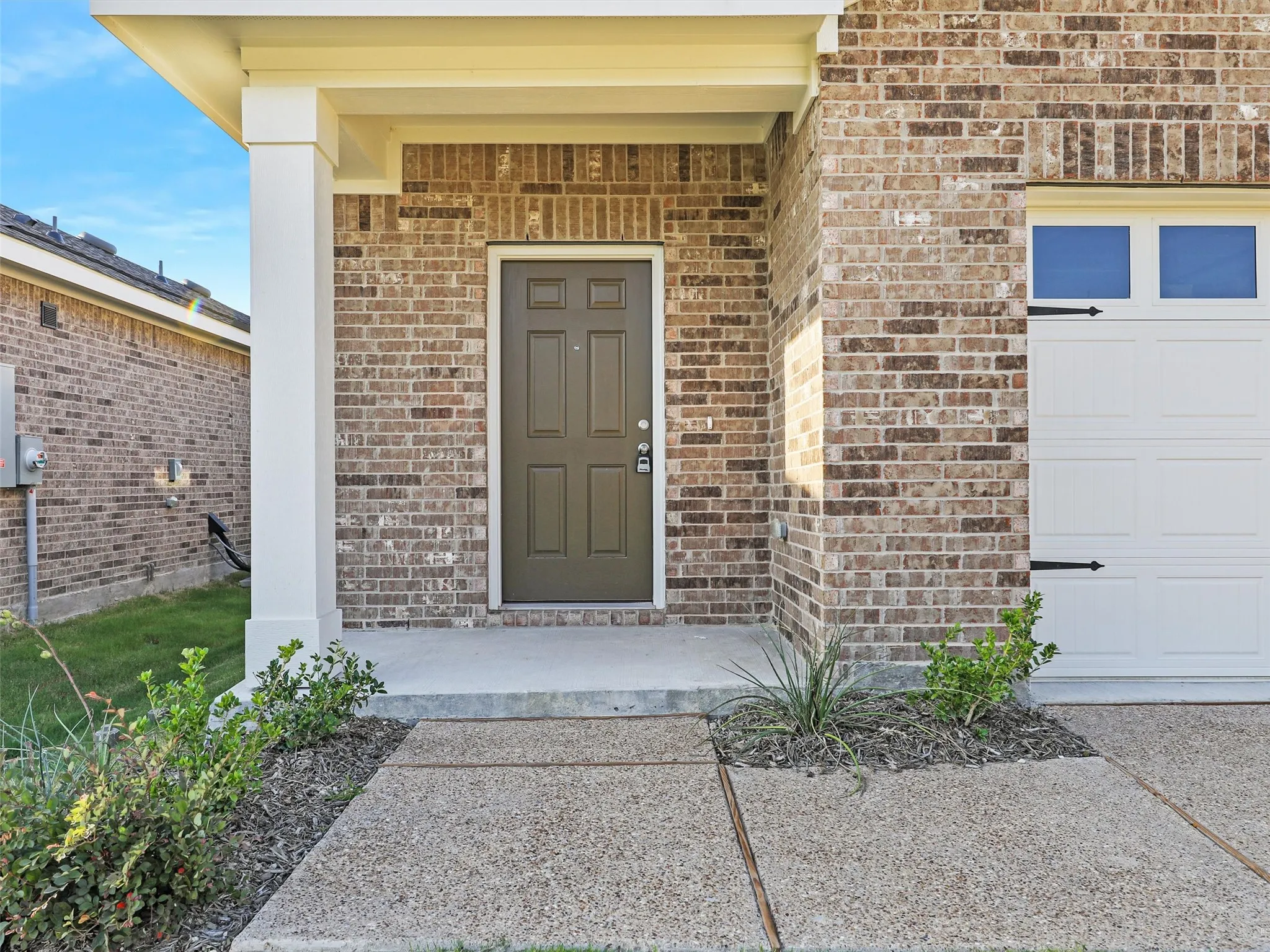 Brick exterior featuring a covered front porch with a white column, a dark paneled entry door, and an attached garage with a white panel door
