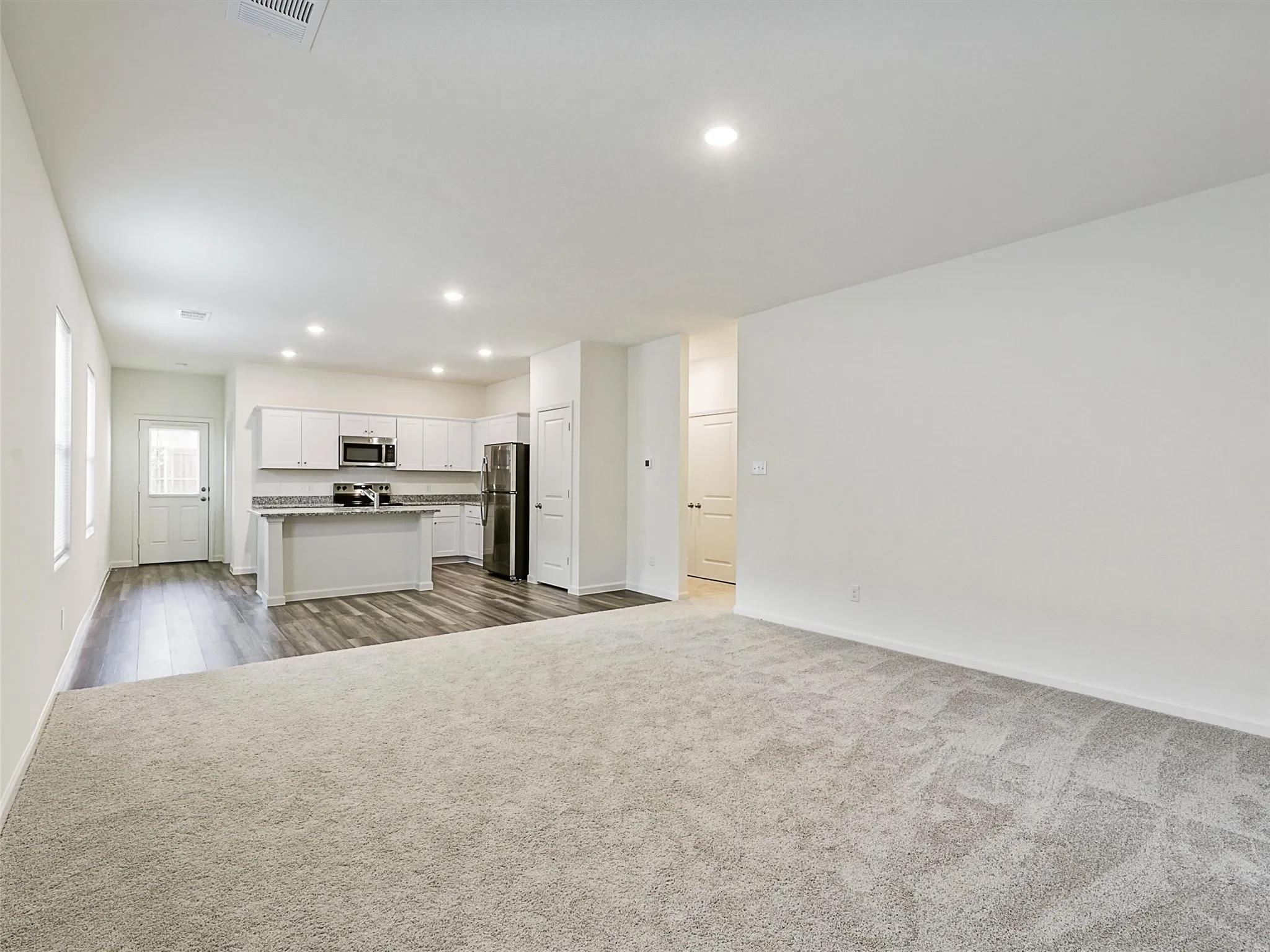 Spacious open-concept living area featuring light-toned carpeting and recessed lighting