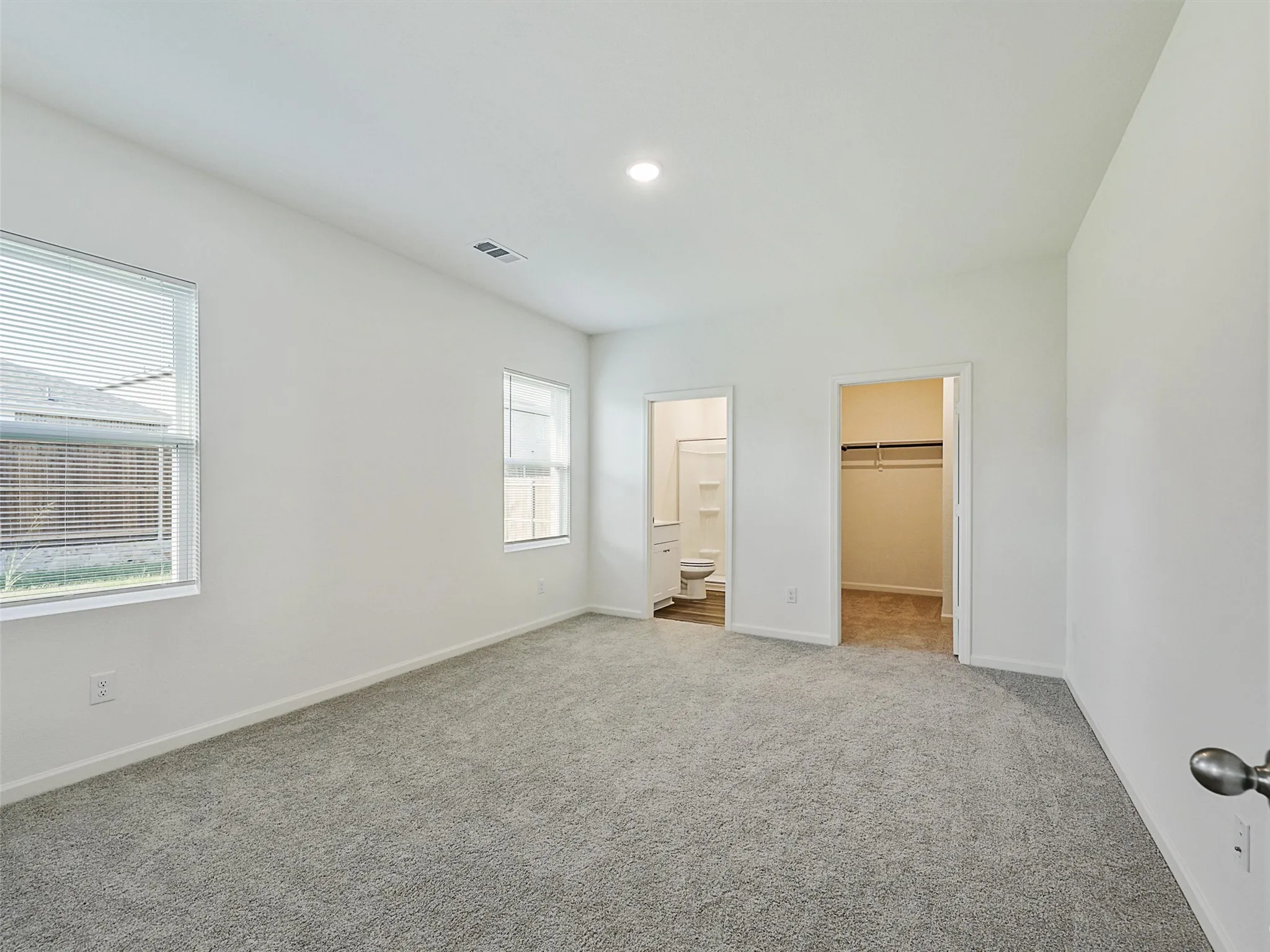 Spacious room featuring neutral carpeting, two windows with blinds, a walk-in closet, and an attached full bathroom