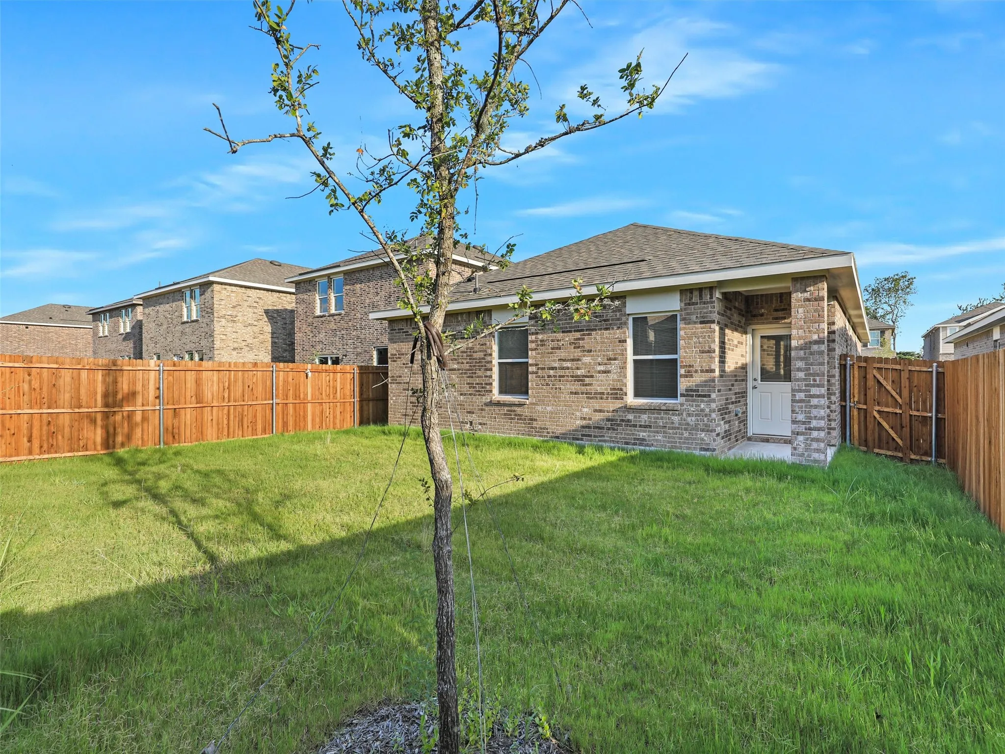 Rear exterior featuring a covered porch entry, brick siding, a brown shingle roof, and a wood privacy fence