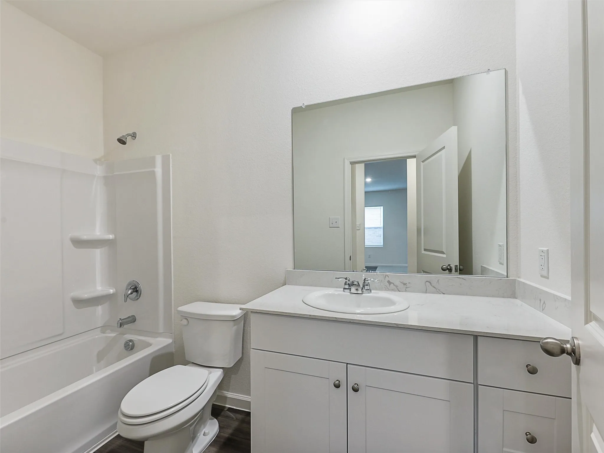 Bathroom featuring a white vanity with a light-colored countertop, an undermount sink with a chrome faucet, a large frameless mirror, a white toilet, and a white tub and shower combination with chrome fixtures