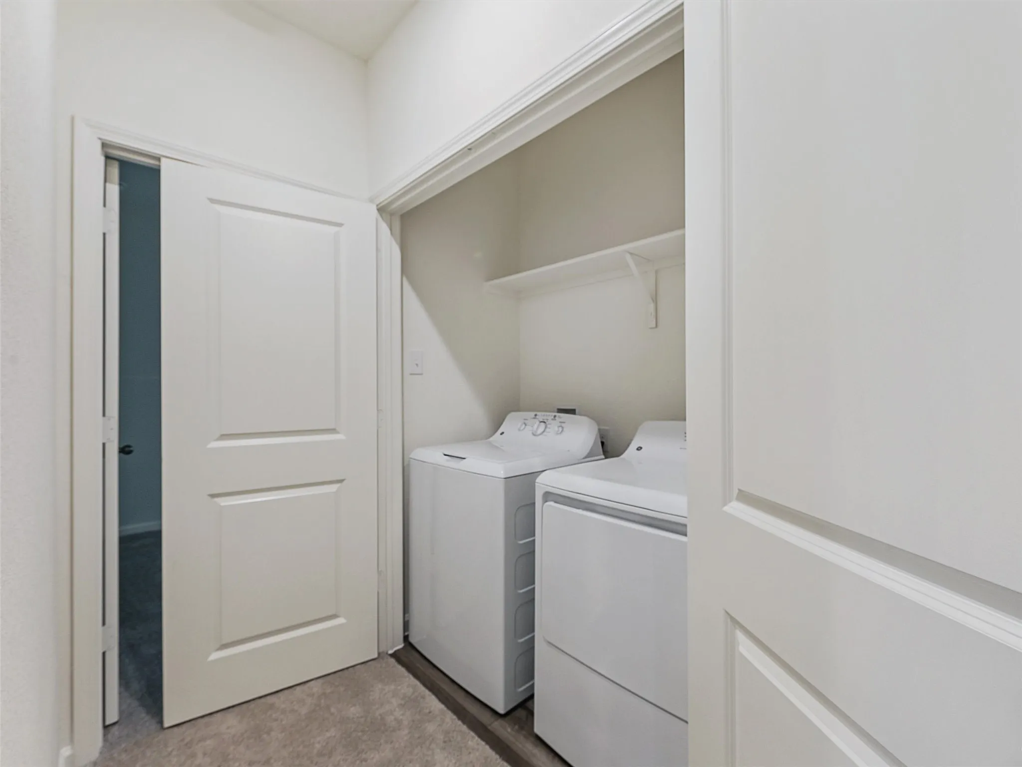 Dedicated laundry closet featuring a built-in shelf, neutral wall tones, and wood-finish flooring