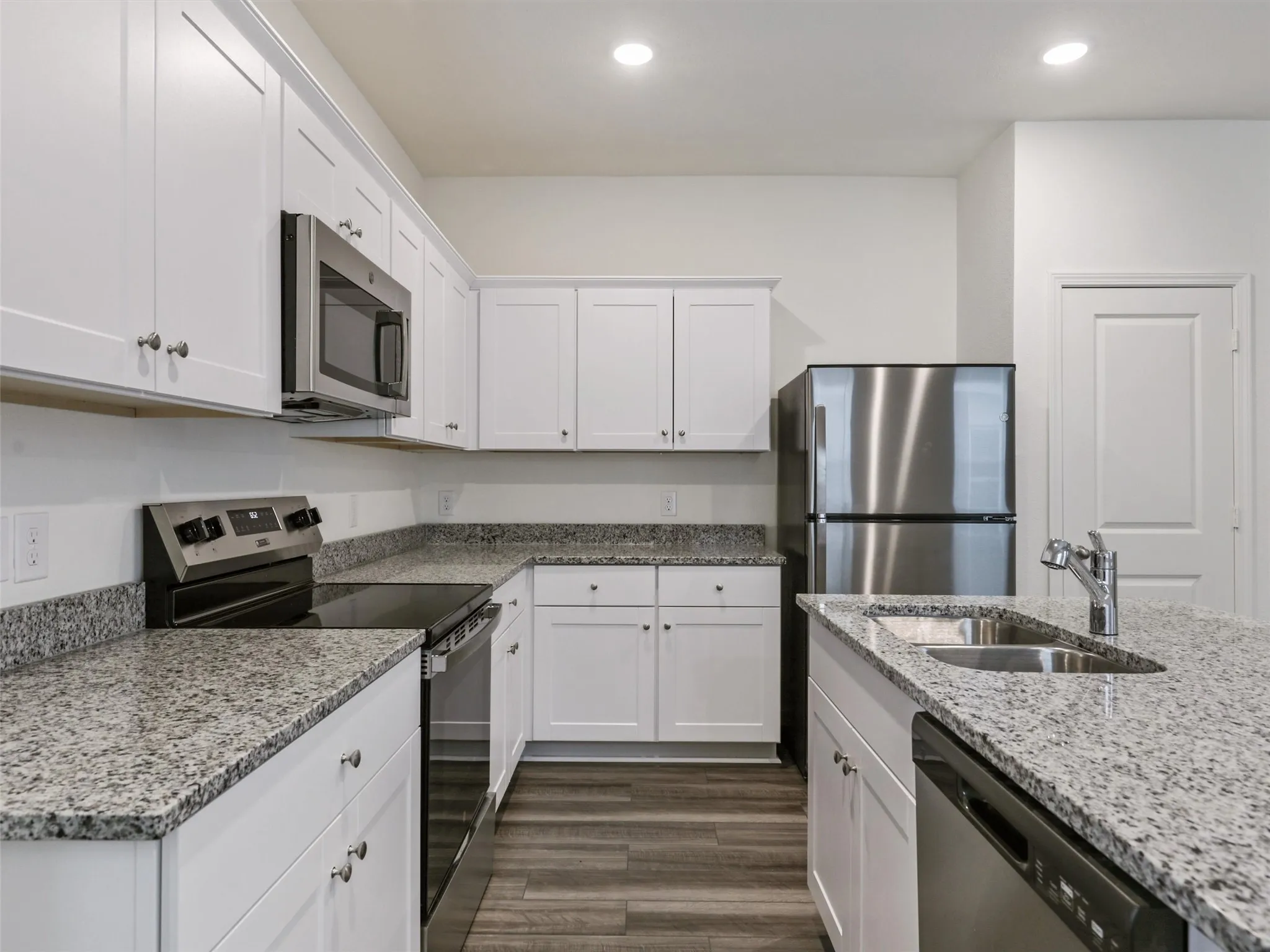 Kitchen featuring white shaker-style cabinetry, speckled countertops, stainless steel appliances, and wood-finish flooring
