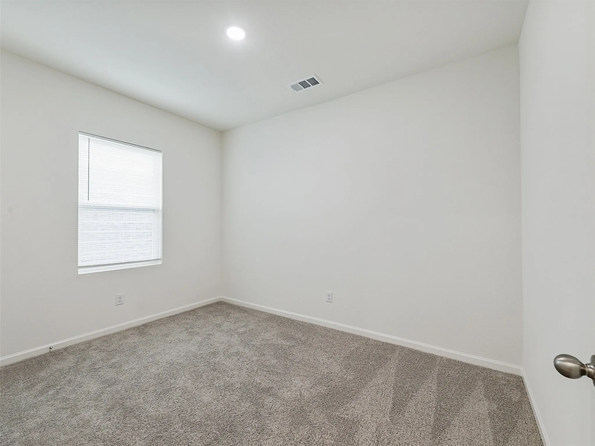 Neutral interior featuring light gray carpet, white walls, a single window with blinds, and recessed lighting