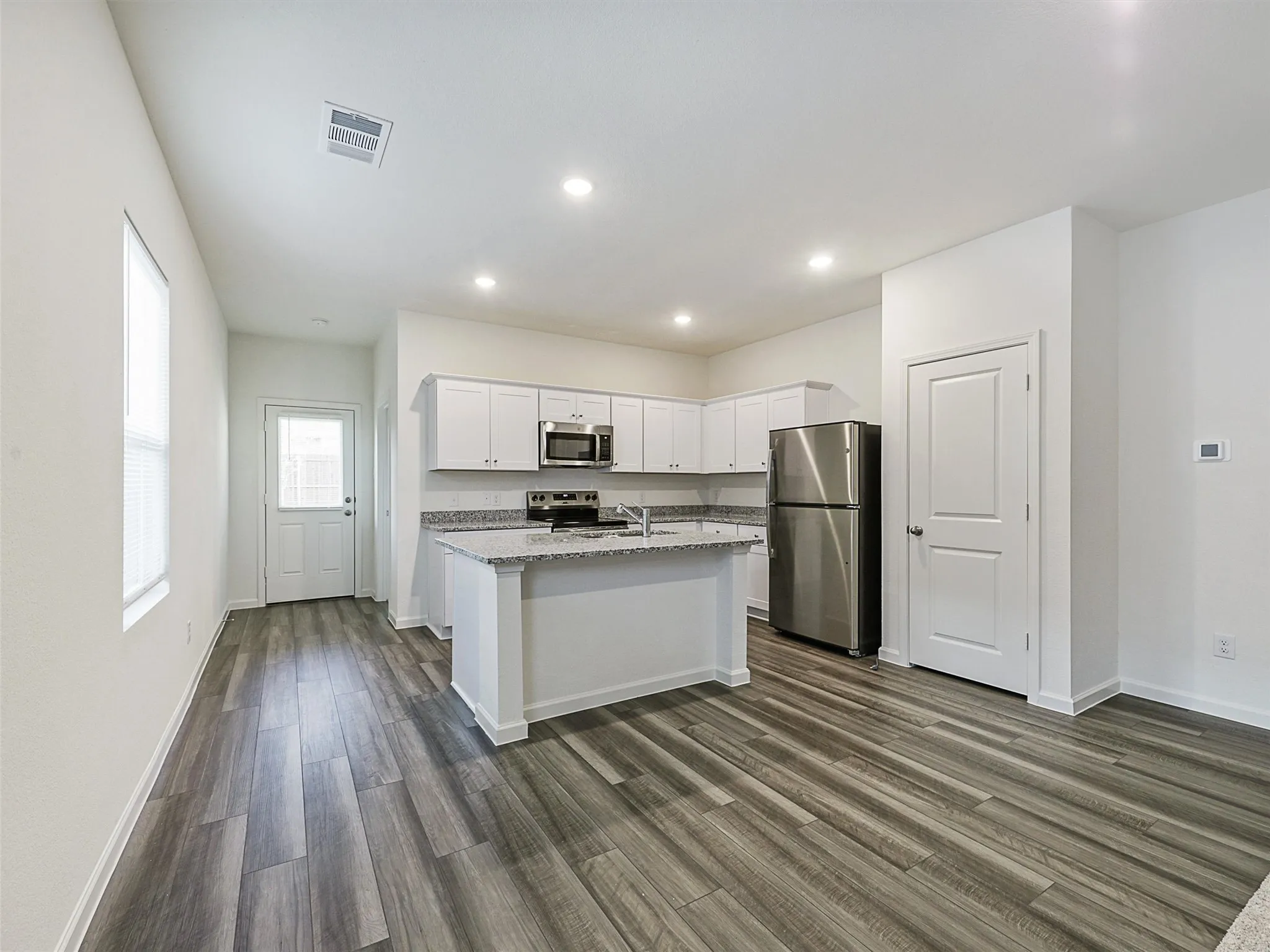 Open-concept kitchen featuring white cabinetry, stainless steel appliances, granite countertops, a kitchen island, and wood-finish flooring