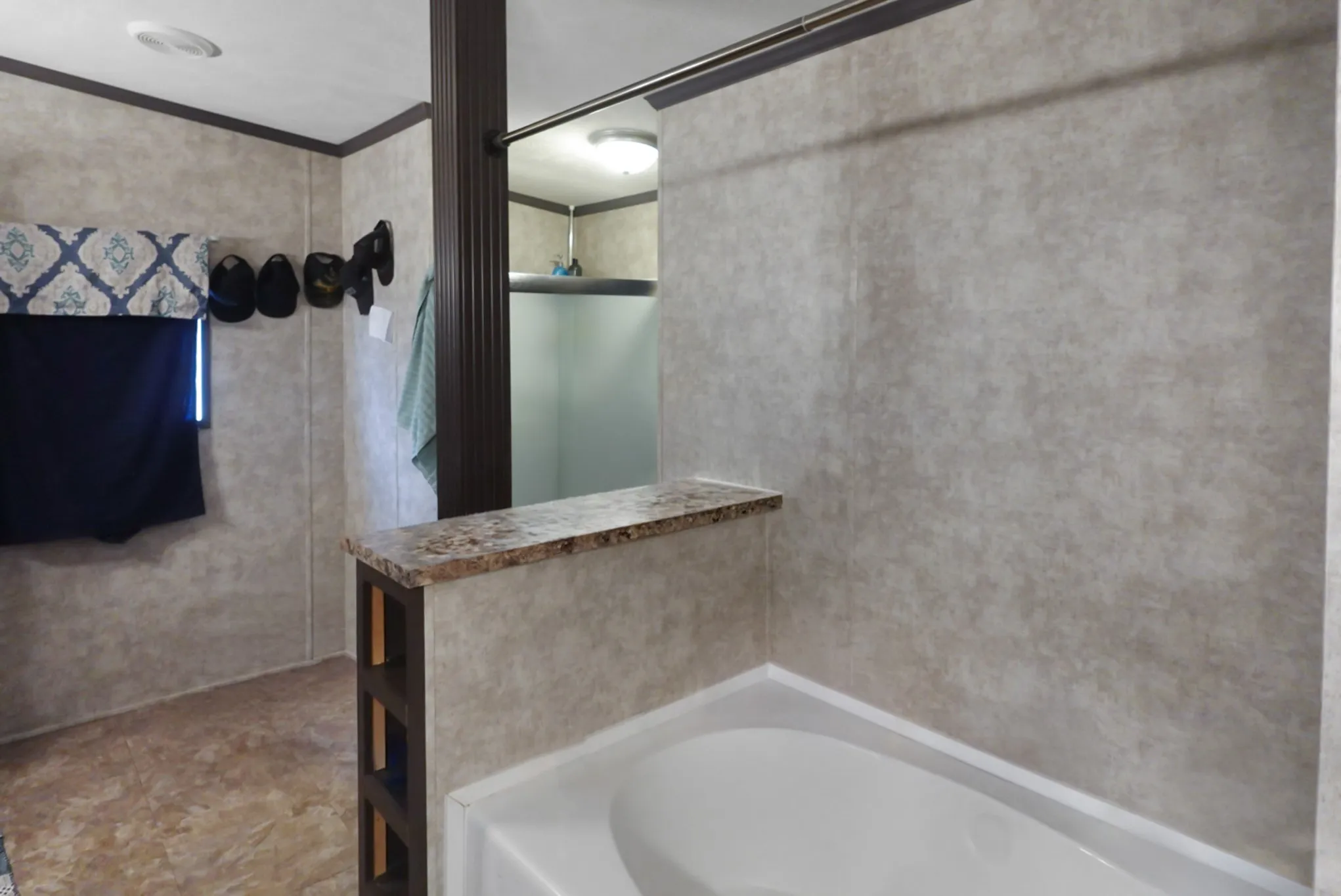 Full-size bathtub with a stone-look shelf, wood-finish trim, and vinyl wall panels