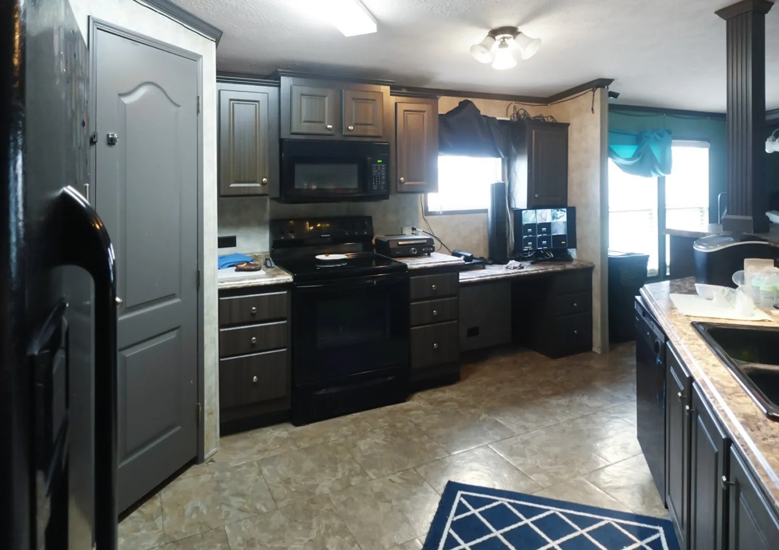 Kitchen featuring dark wood-finish cabinetry, black appliances, a built-in desk area, and light-toned flooring