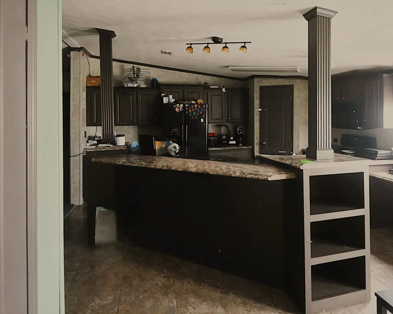 Kitchen featuring dark cabinetry, a built-in island with storage shelves, and a dark countertop