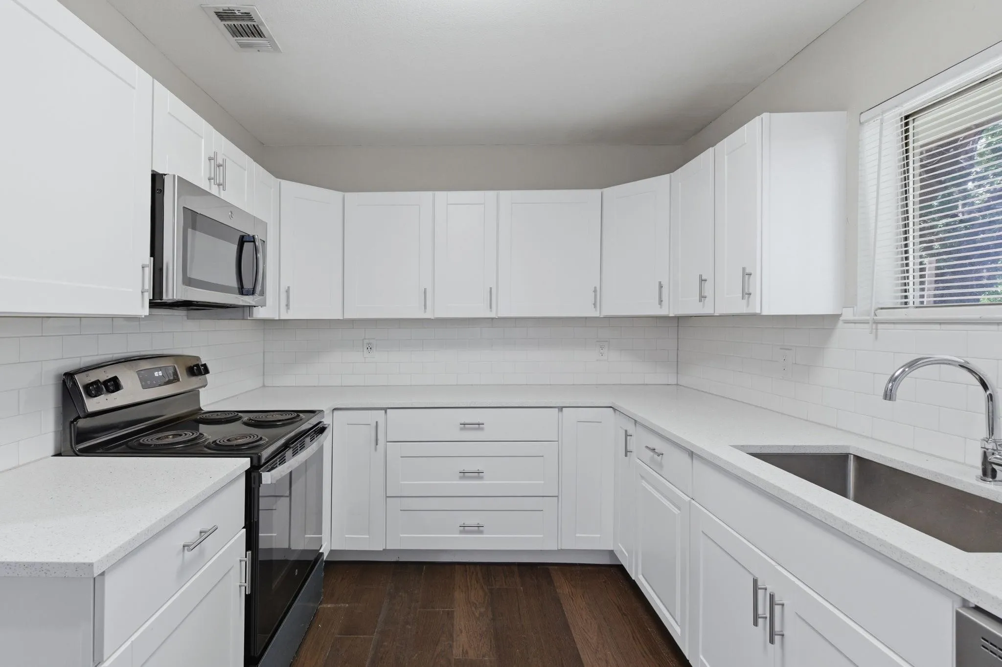 Contemporary kitchen featuring white cabinetry, light countertops, stainless steel appliances, a subway tile backsplash, and wood-finish flooring
