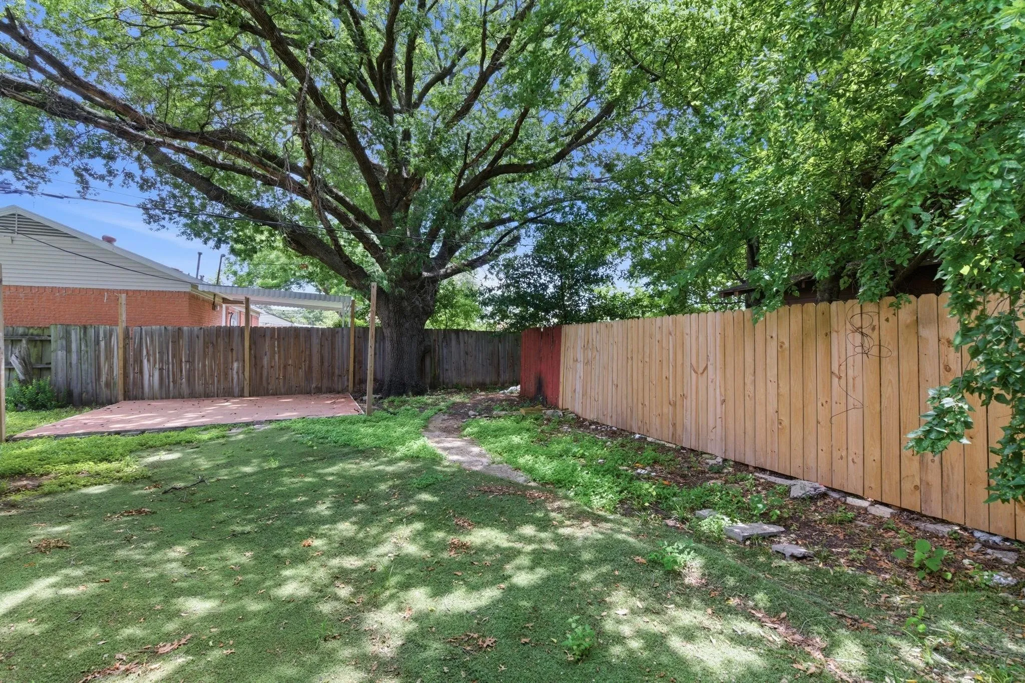 Expansive backyard featuring a mature shade tree, a new wood privacy fence, and a concrete patio pad