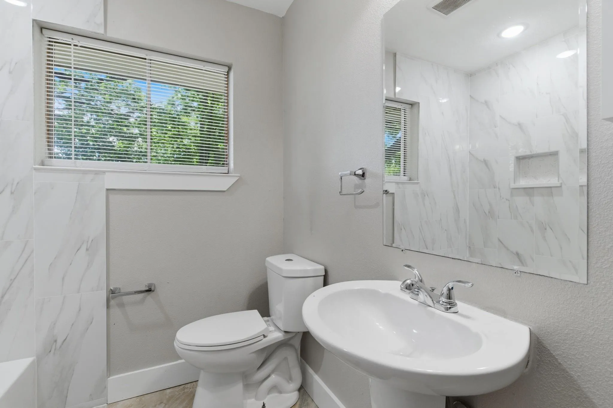 Bathroom featuring a pedestal sink with chrome fixtures, a toilet, and a window with blinds