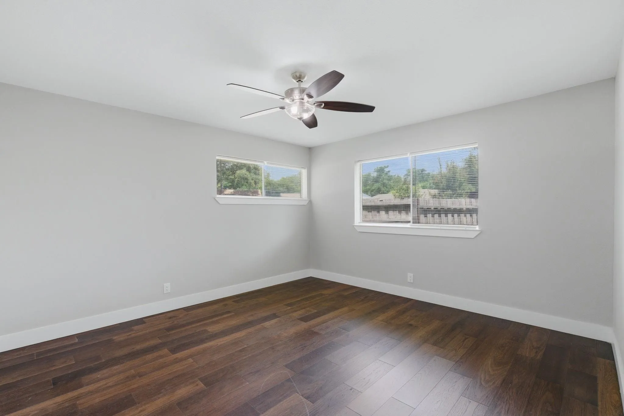 Room featuring rich wood-finish flooring, light gray walls, white baseboards, and a modern ceiling fan with integrated lighting