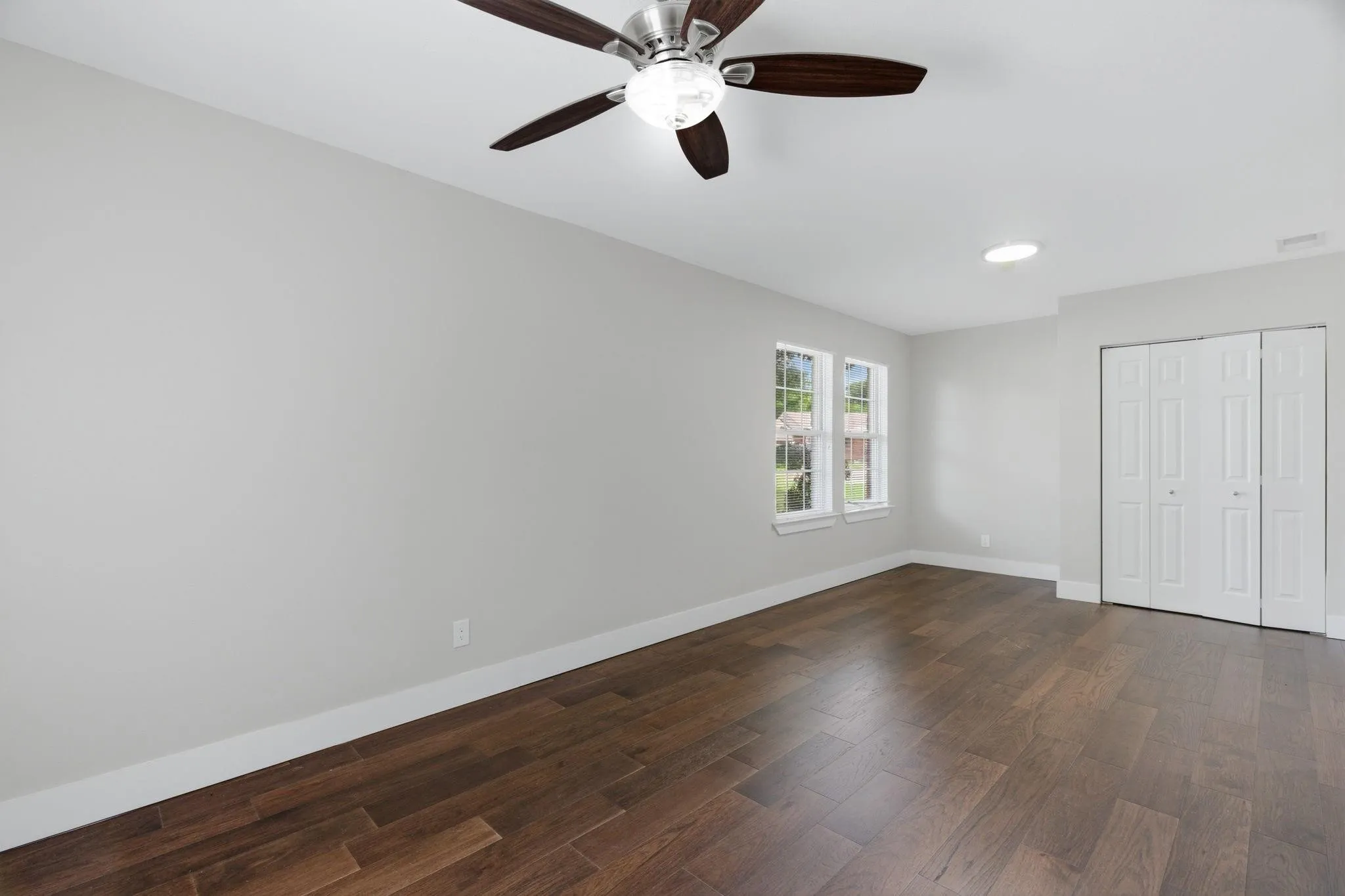 Spacious room featuring wood-finish flooring, light gray walls, white trim, and a ceiling fan with integrated lighting