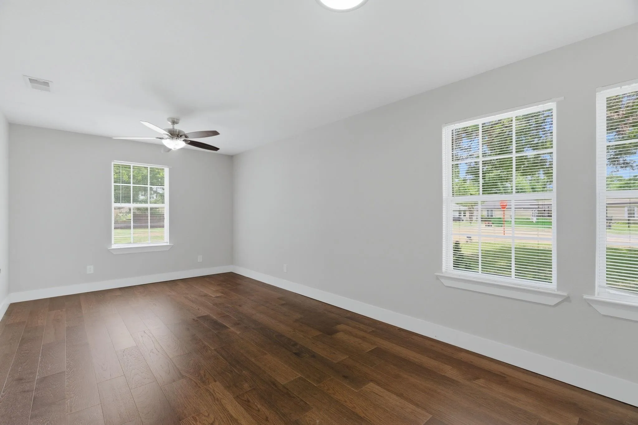 Spacious room featuring rich wood-finish flooring, light gray walls, and white trim