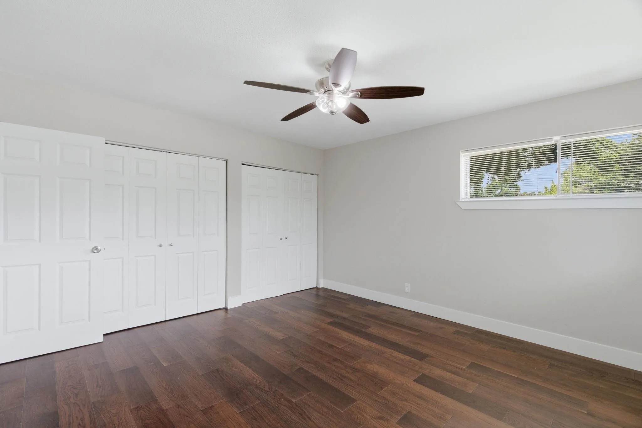 Room featuring wood-finish flooring, a ceiling fan with integrated lighting, and a horizontal window with blinds