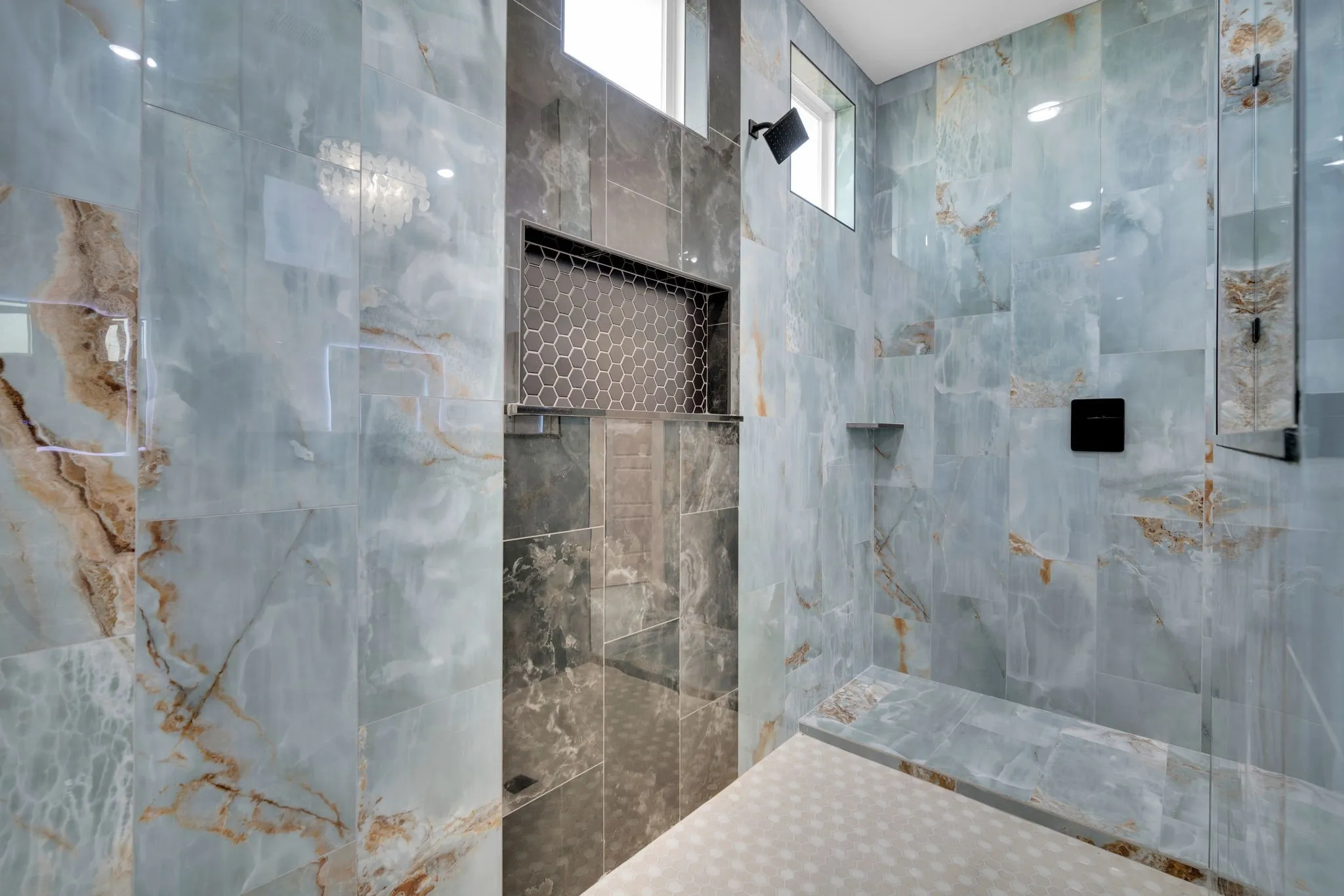 Luxurious primary bathroom showcasing expansive tile walls with natural stone veining in soft gray and taupe tones
