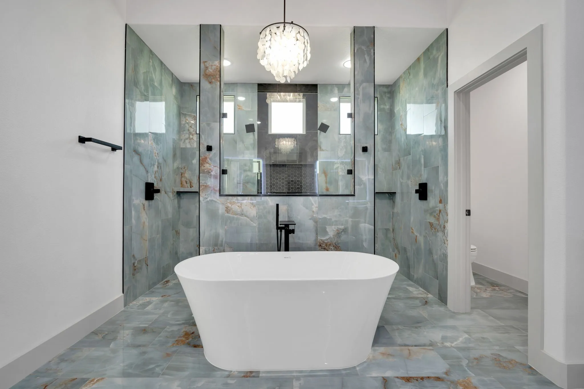 Freestanding soaking tub centered in a bathroom featuring full-height blue-hued stone tile walls and flooring