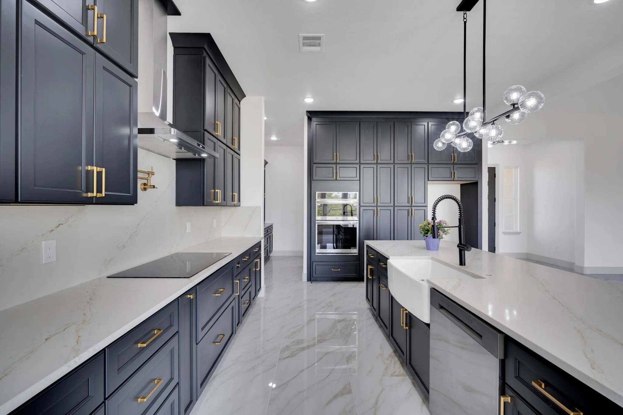 Gourmet kitchen with dark cabinetry, quartz countertops, a large center island featuring a farmhouse sink, stainless steel appliances, and a modern chandelier