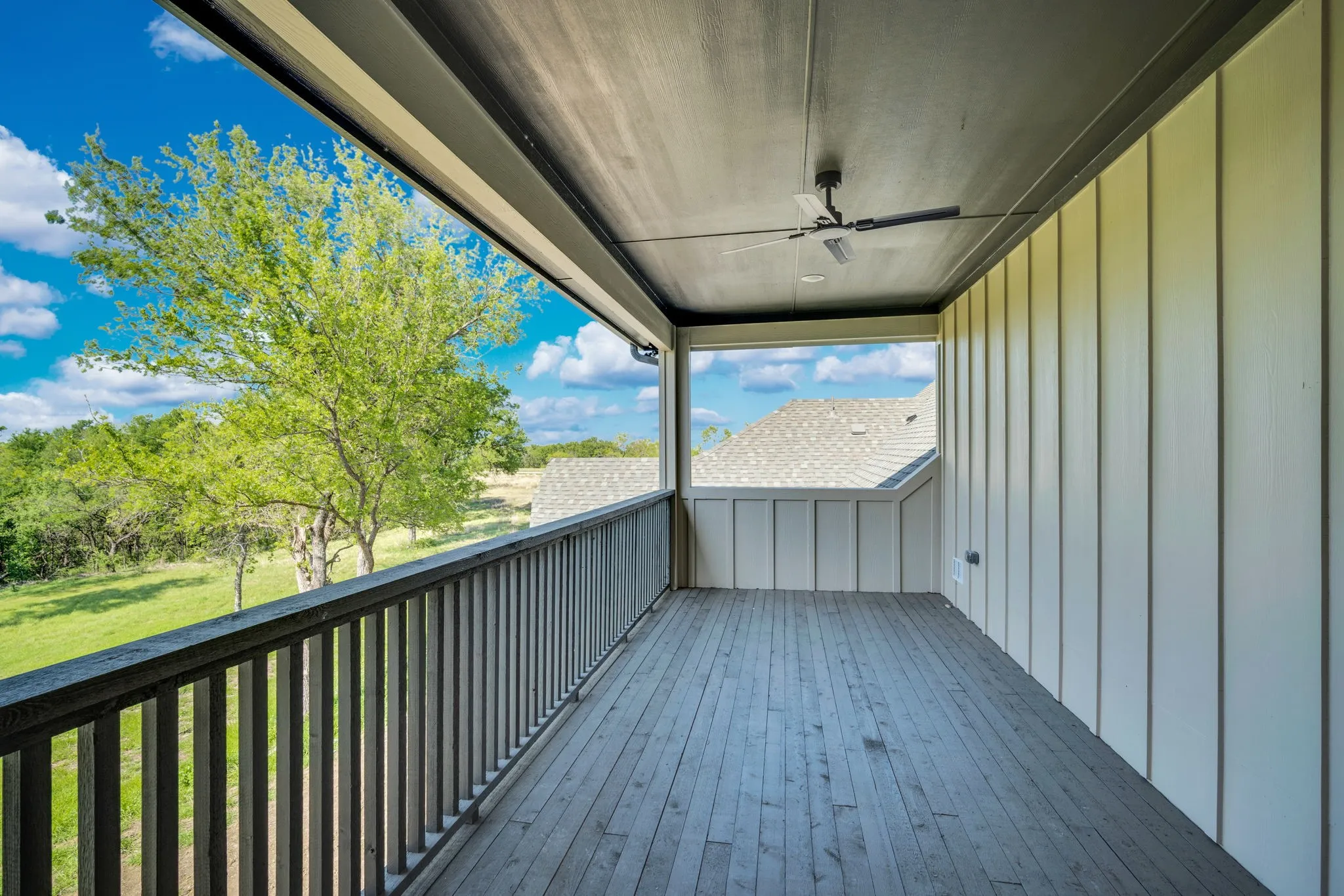 Covered deck featuring composite decking, metal railing, and ceiling fan, overlooking mature landscaping and open grounds