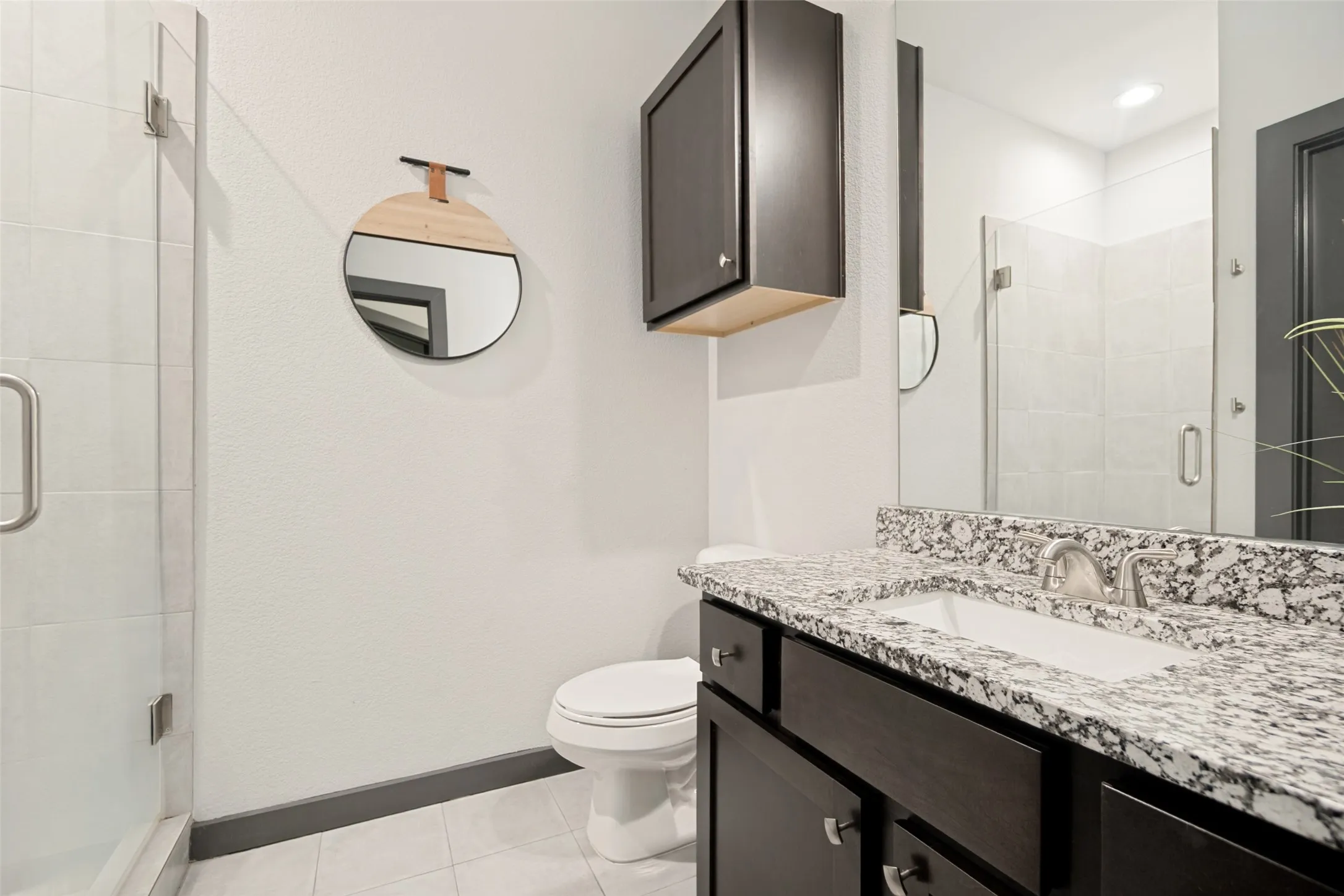 Bathroom featuring a frameless glass shower enclosure, a single vanity with a white rectangular sink, a speckled countertop, dark wood-finish cabinetry, and a wall-mounted medicine cabinet