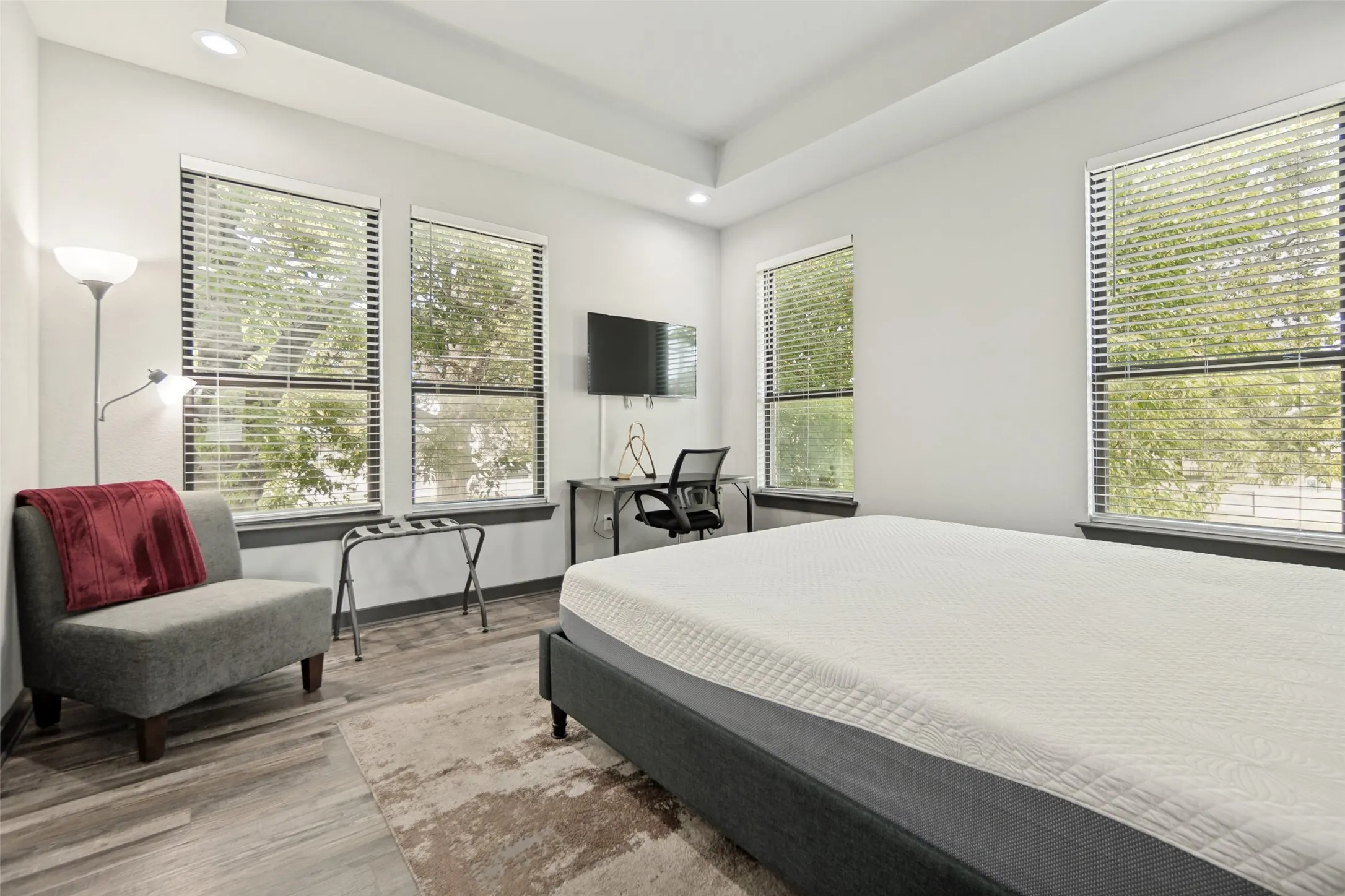 Bright room featuring three large windows with blinds, wood-finish flooring, and a tray ceiling with recessed lighting