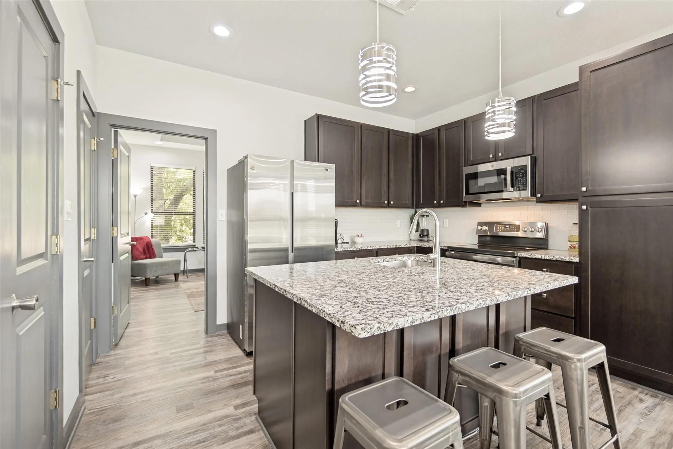 Contemporary kitchen featuring dark wood cabinetry, stainless steel appliances, a center island with a granite-style countertop, and wood-finish flooring