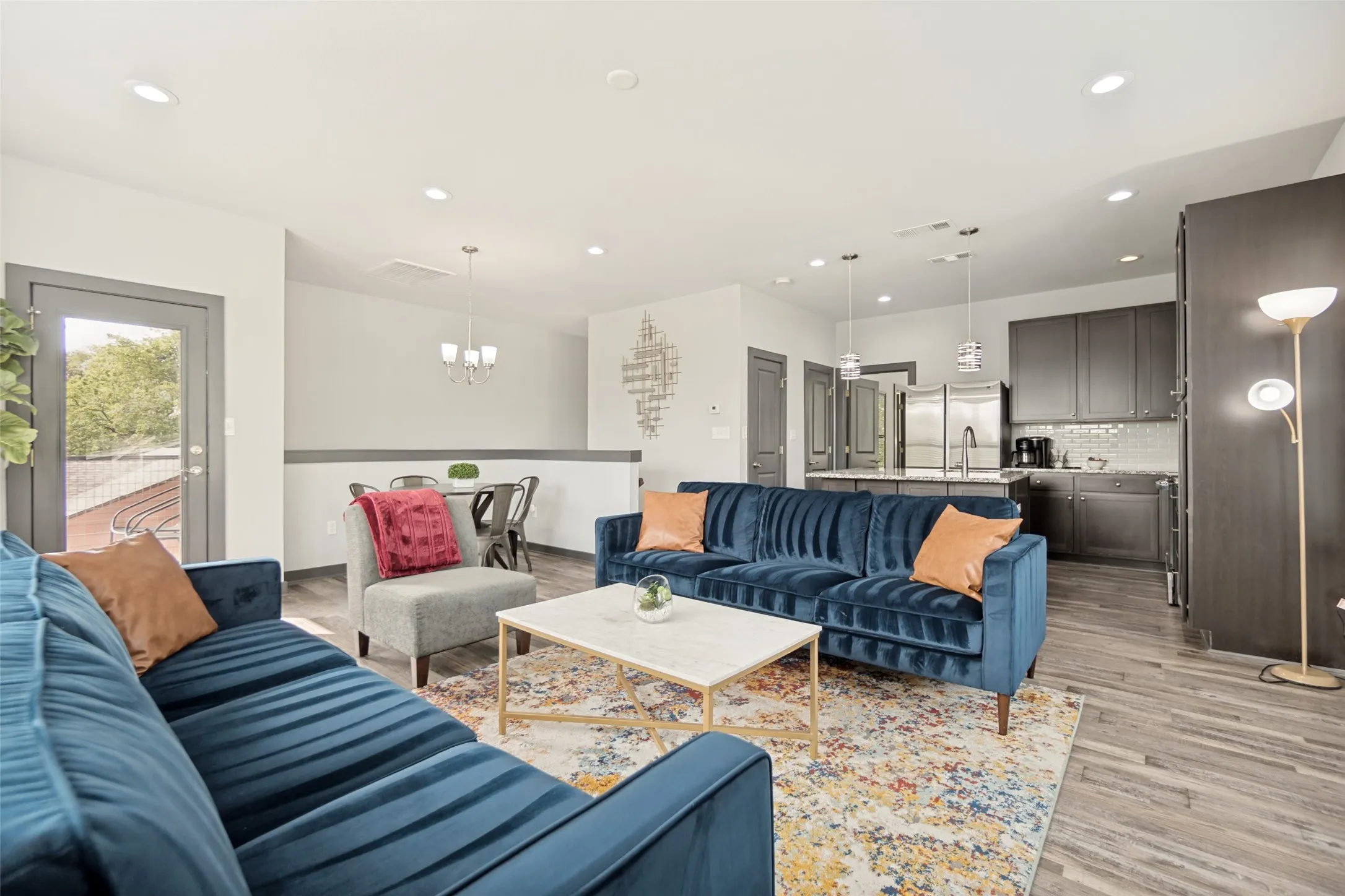 Open-concept living area showcasing multiple seating zones with blue upholstered sofas, wood-finish flooring throughout, and recessed ceiling lighting