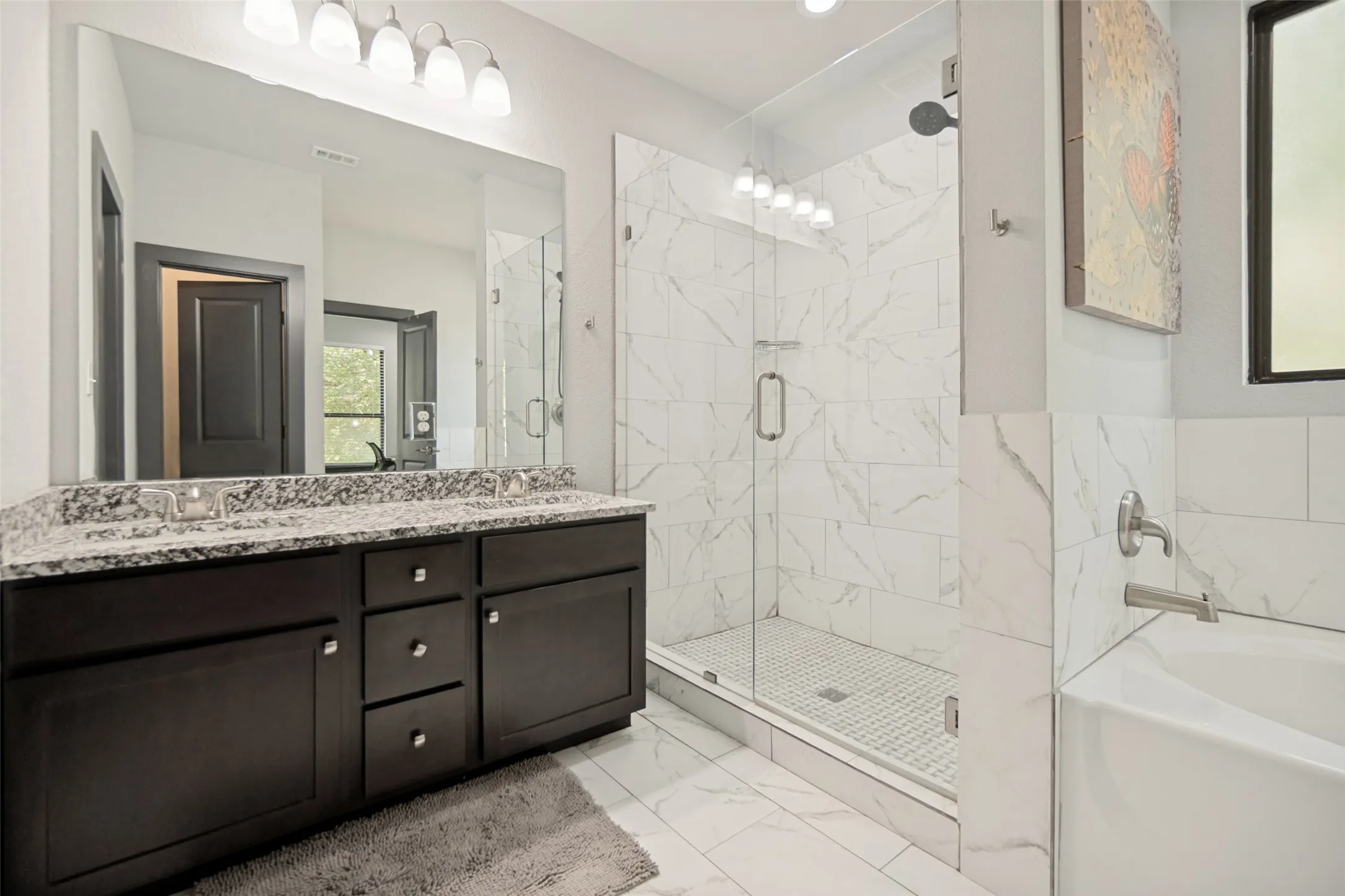 Bathroom featuring a dual vanity with a granite countertop, a frameless glass shower enclosure with marble-look tile, and a built-in soaking tub with brushed nickel fixtures