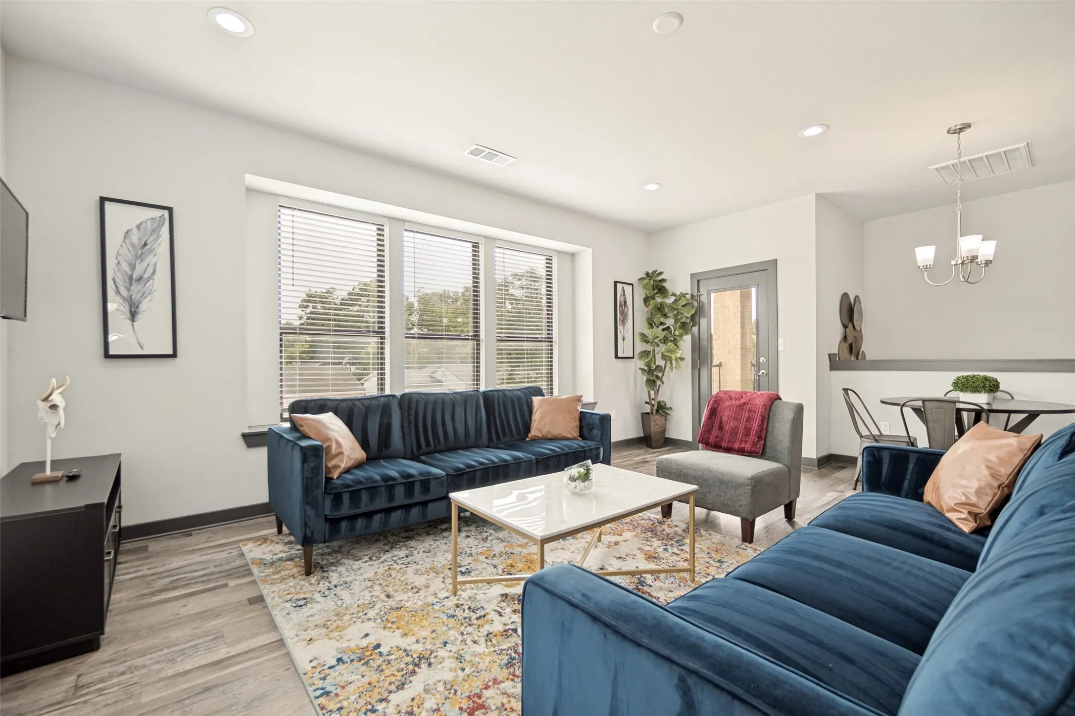 Open-concept living area featuring wood-finish flooring, recessed lighting, and large windows with blinds