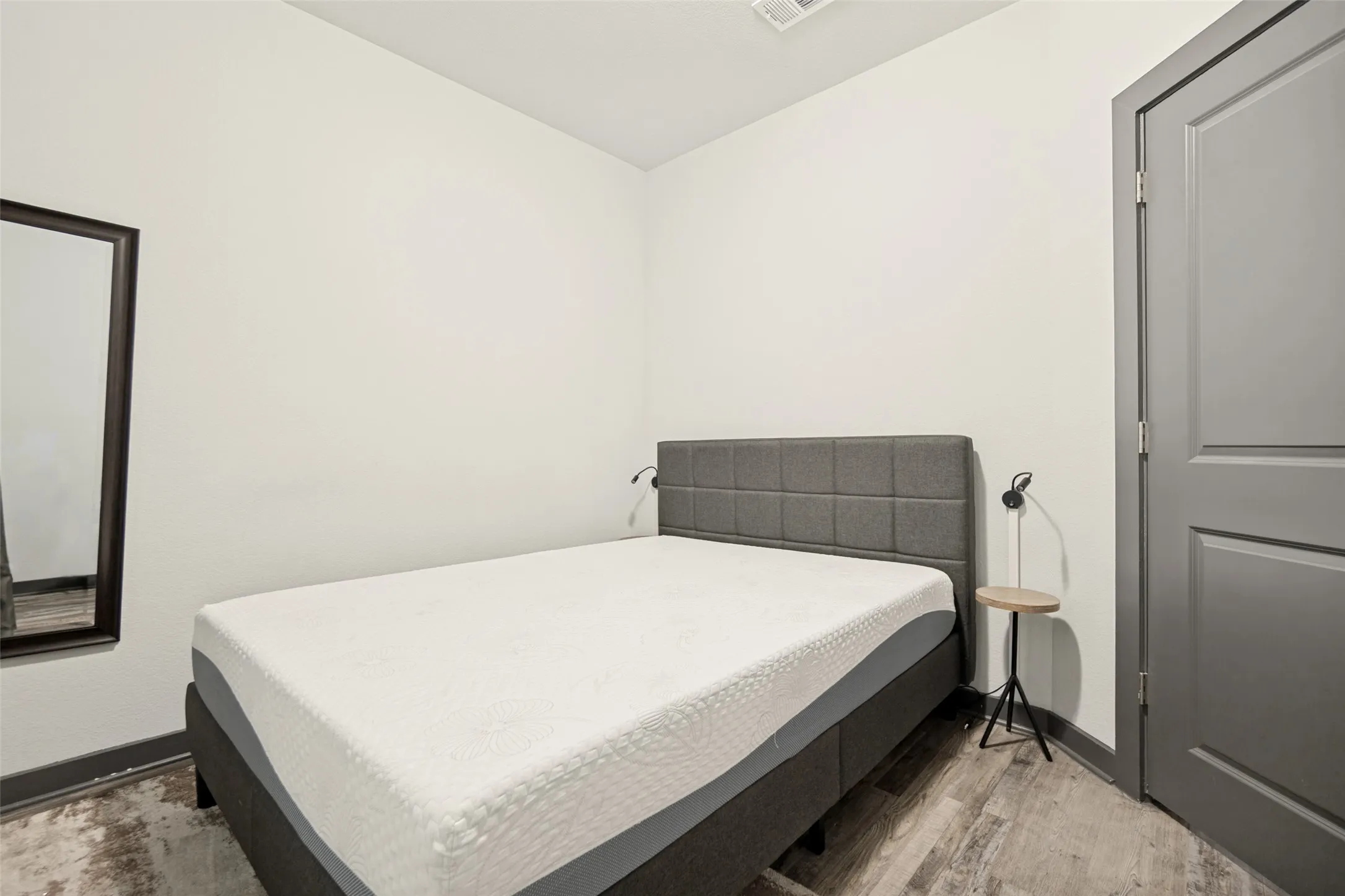 Bedroom featuring light grey walls, wood-finish flooring, and a grey paneled door