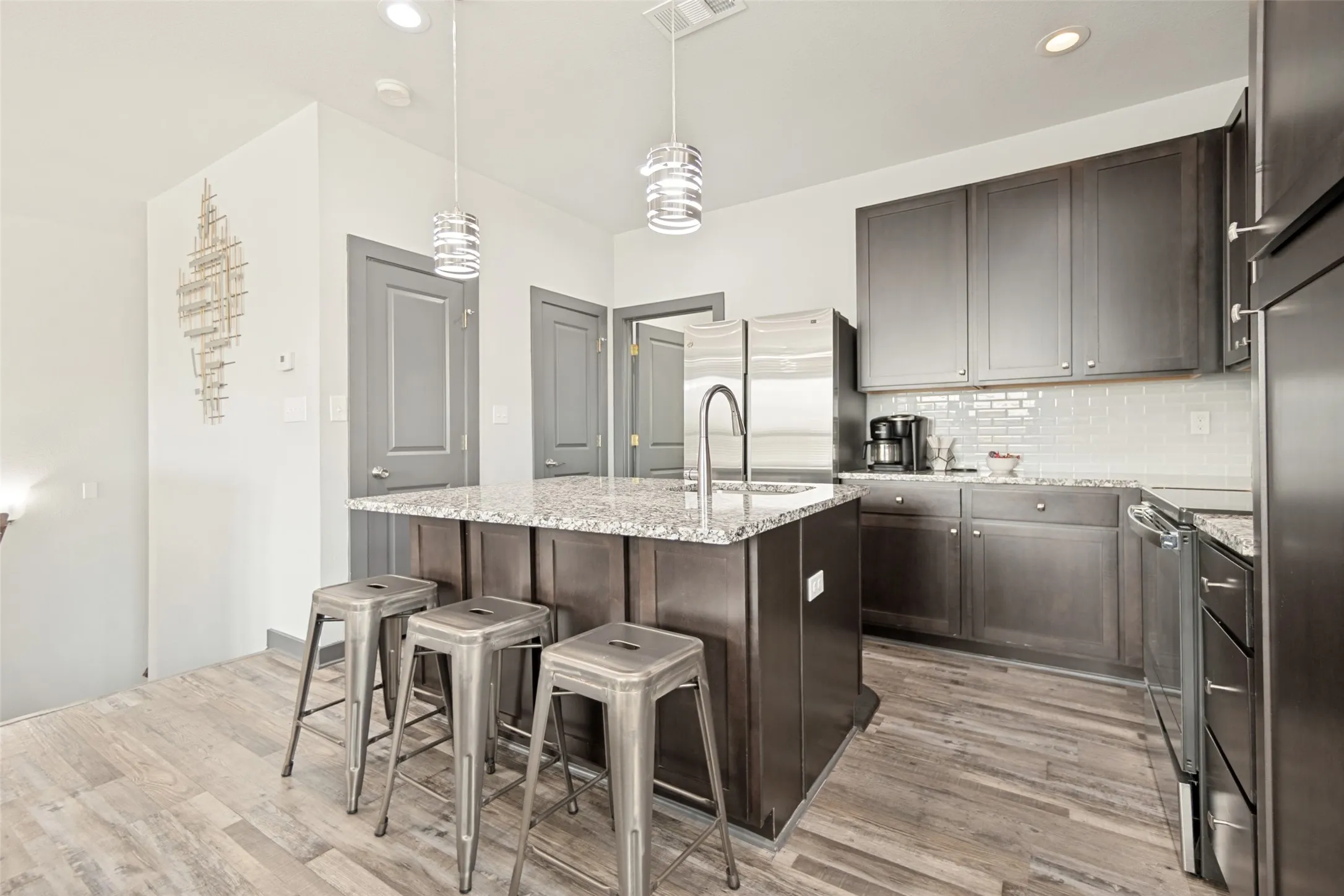 Modern kitchen featuring a dark cabinetry suite with stainless steel appliances, quartz countertops, and a waterfall-edge island with seating for three