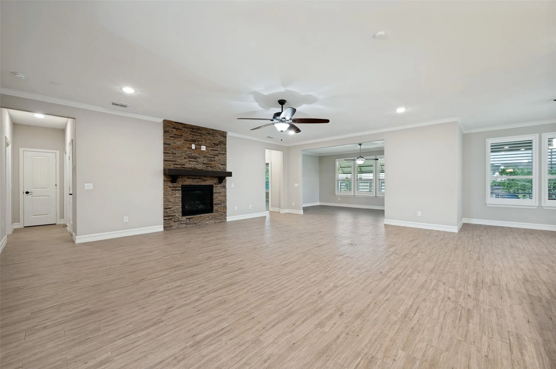 Spacious open-concept living area featuring wood-finish flooring throughout, a brick fireplace with dark surround, recessed lighting, and ceiling fan