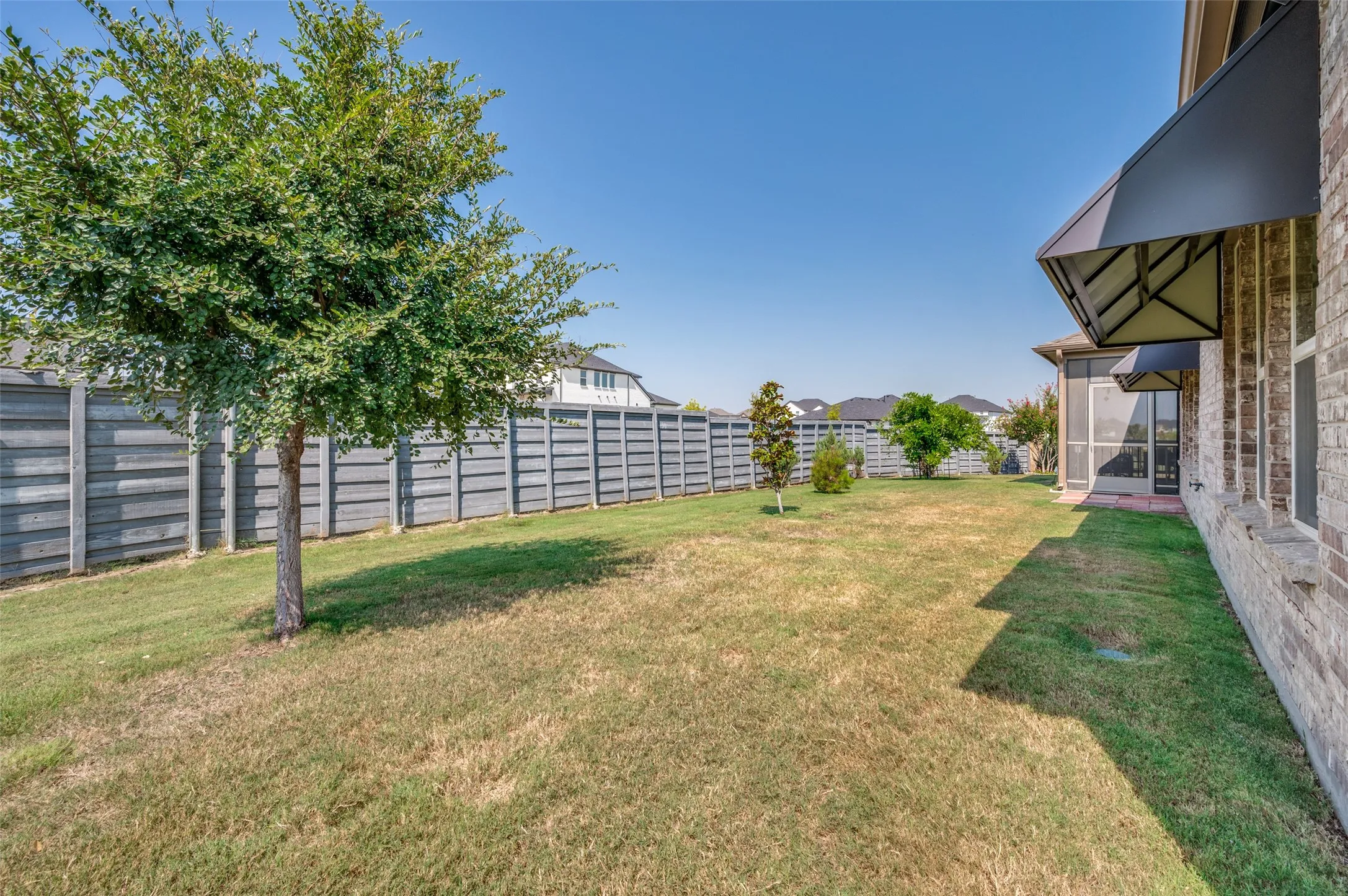 Spacious backyard with mature tree, full privacy fencing, and brick exterior