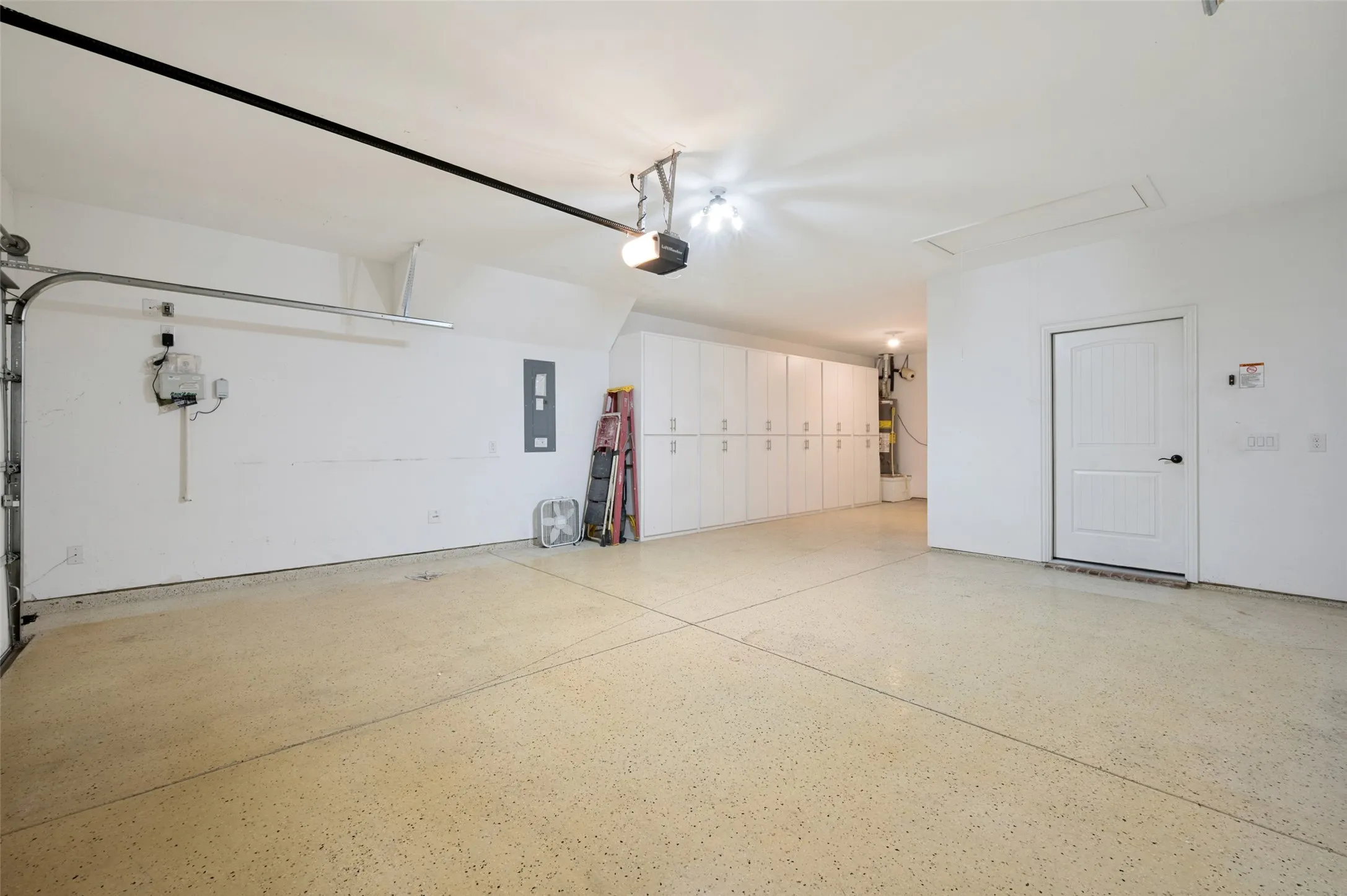 Spacious garage featuring expansive built-in cabinetry, an overhead garage door, a side door entry, and a textured concrete floor