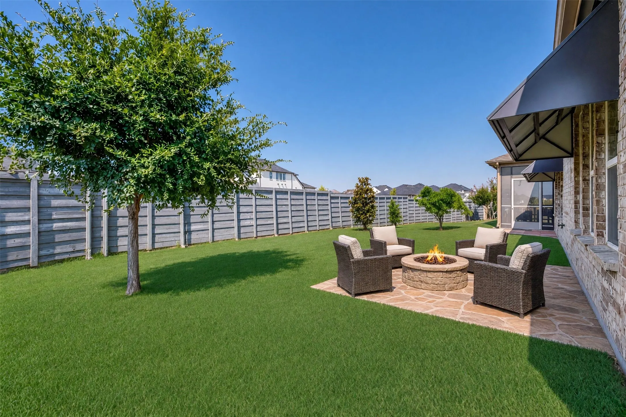 Expansive backyard featuring a stone patio, a built-in fire pit, and a screened-in porch with an awning/ Virtually staged