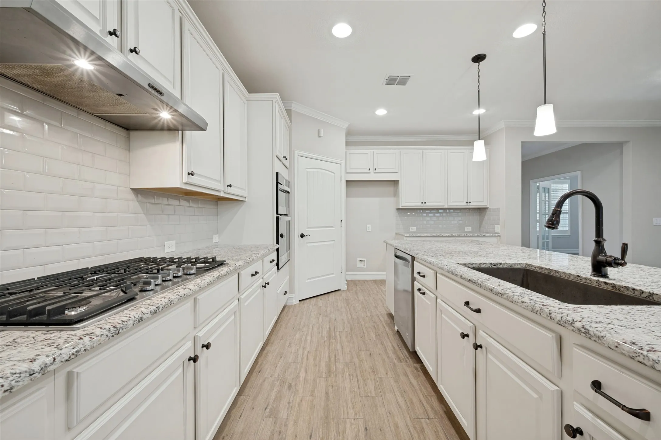 Galley kitchen featuring white cabinetry with hardware accents, quartz countertops, subway tile backsplash, gas cooktop, stainless steel appliances, pendant lighting, and wood-finish flooring throughout