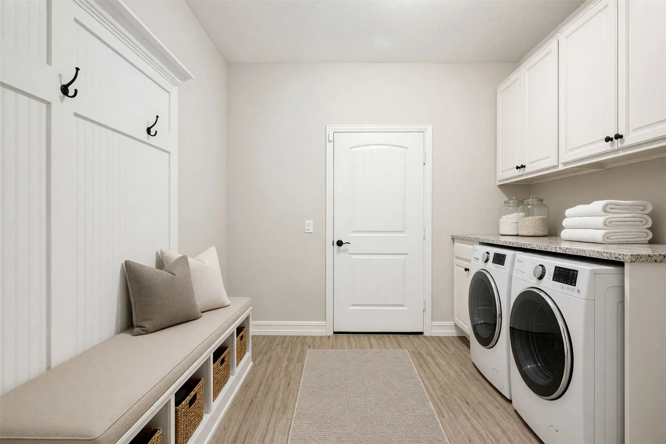 Laundry area featuring a built-in bench with storage, white upper cabinetry, wood-finish flooring, and a countertop