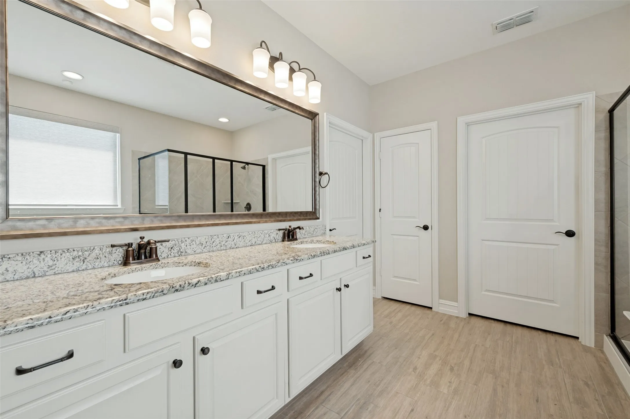 Double vanity featuring white cabinetry, granite countertops, and dual undermount sinks with bronze-finish fixtures