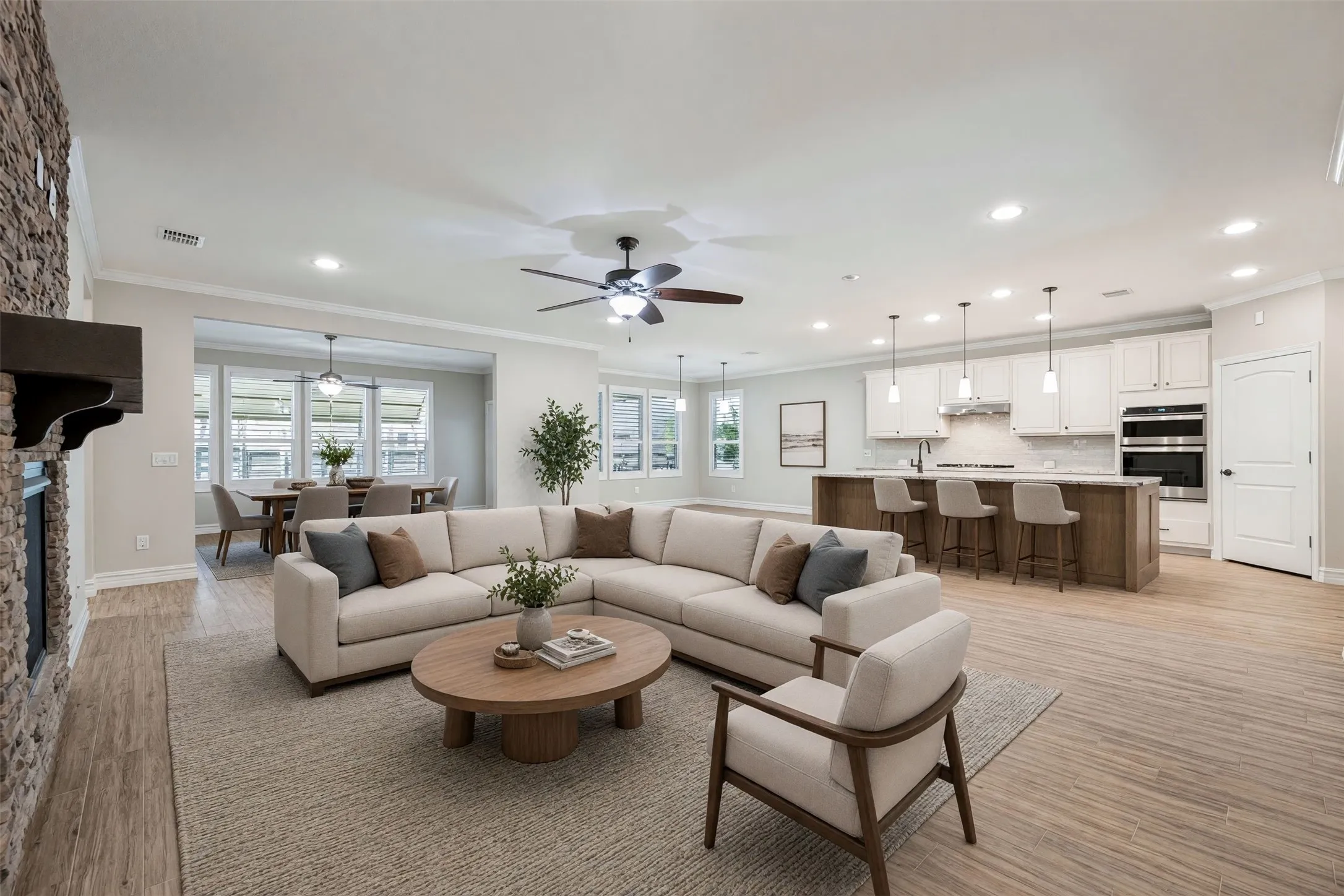 Expansive open-concept living area featuring a stone-clad fireplace and wood-finish flooring/Virtually staged